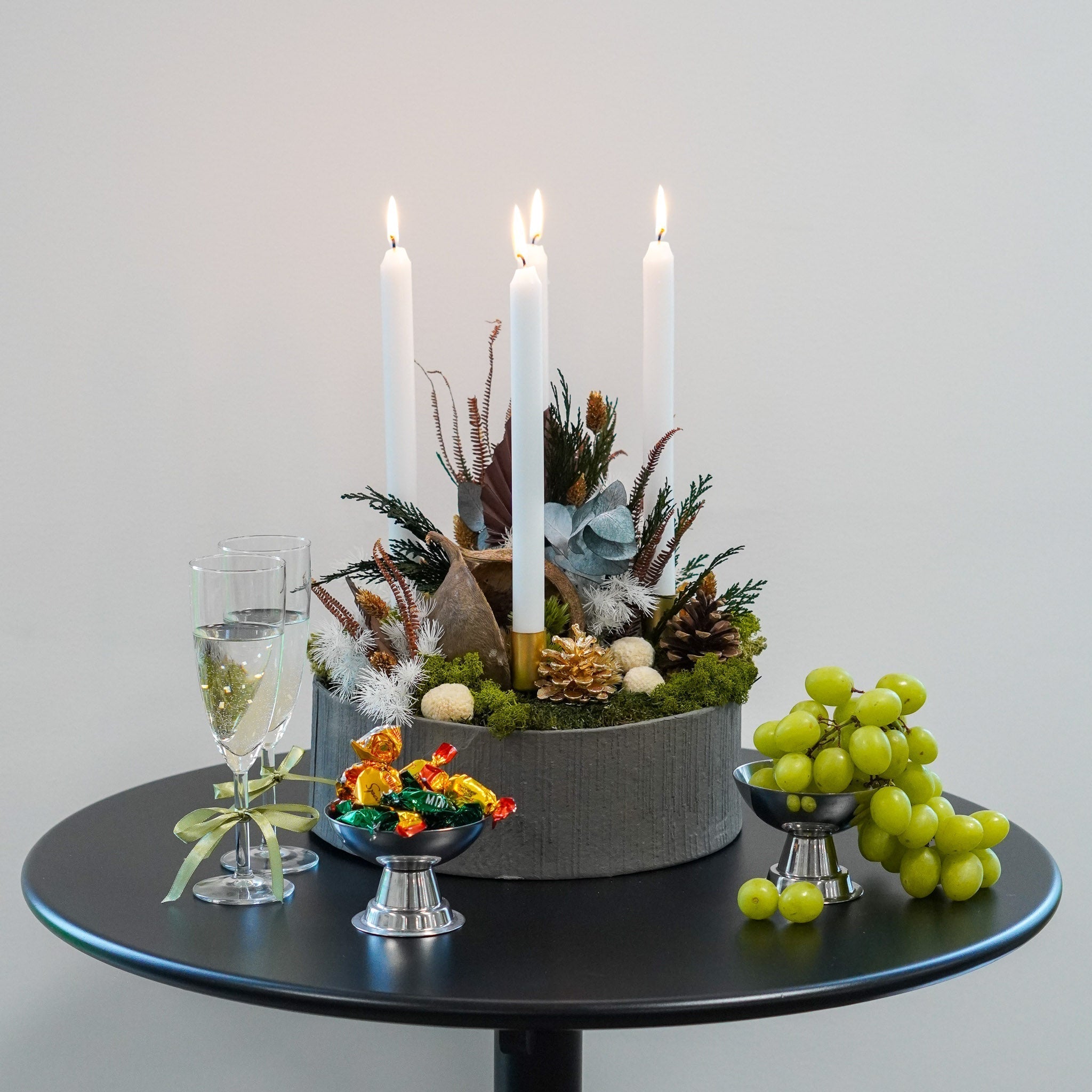 Stämningsfull adventsdekoration med levande ljus, en klase vindruvor och två glas redo för skål.