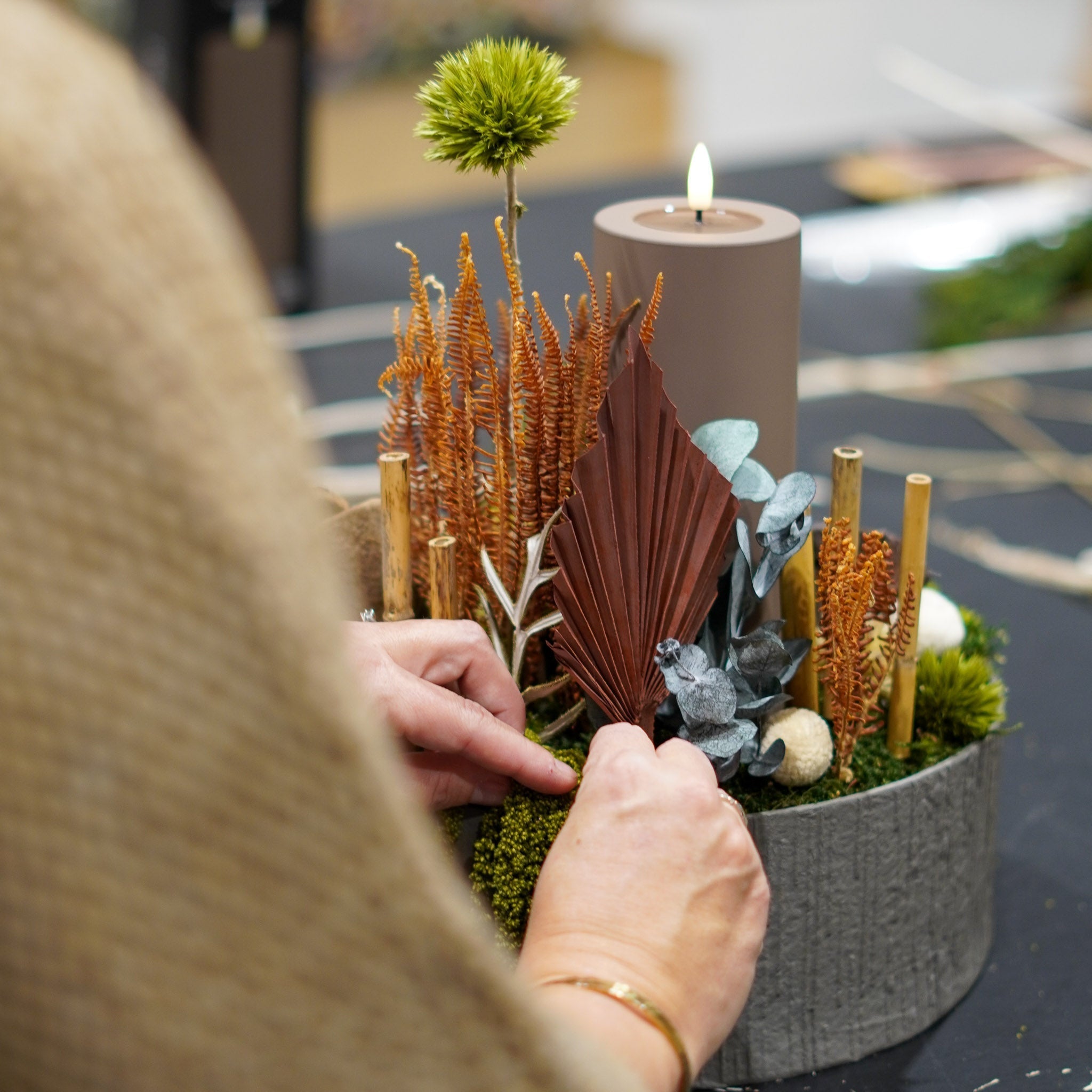 Detaljbild av floristens händer som arrangerar en juldekoration i brunt.