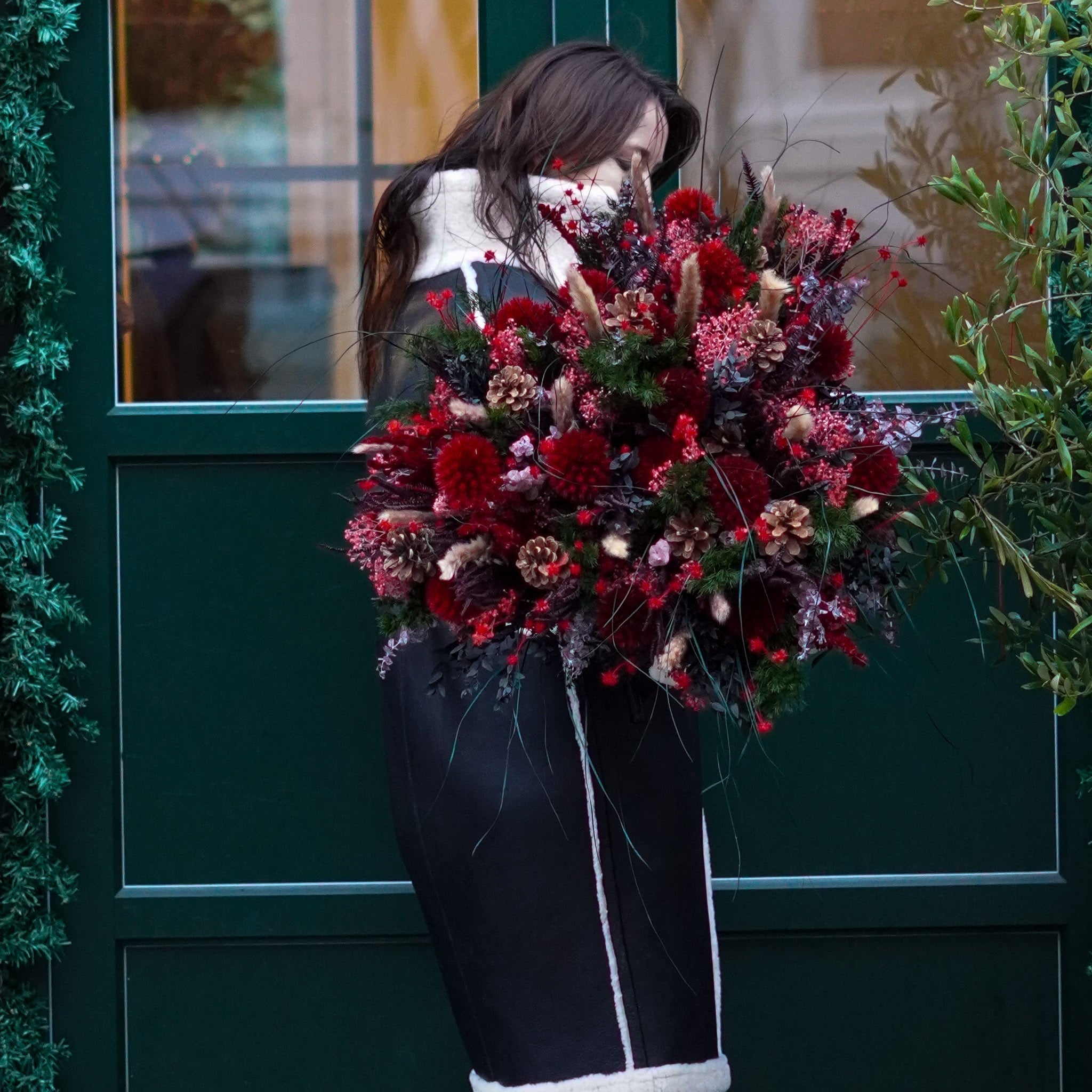 Kvinna står utanför en huvuddörr med en stor, elegant, mörkröd bukett i famnen.