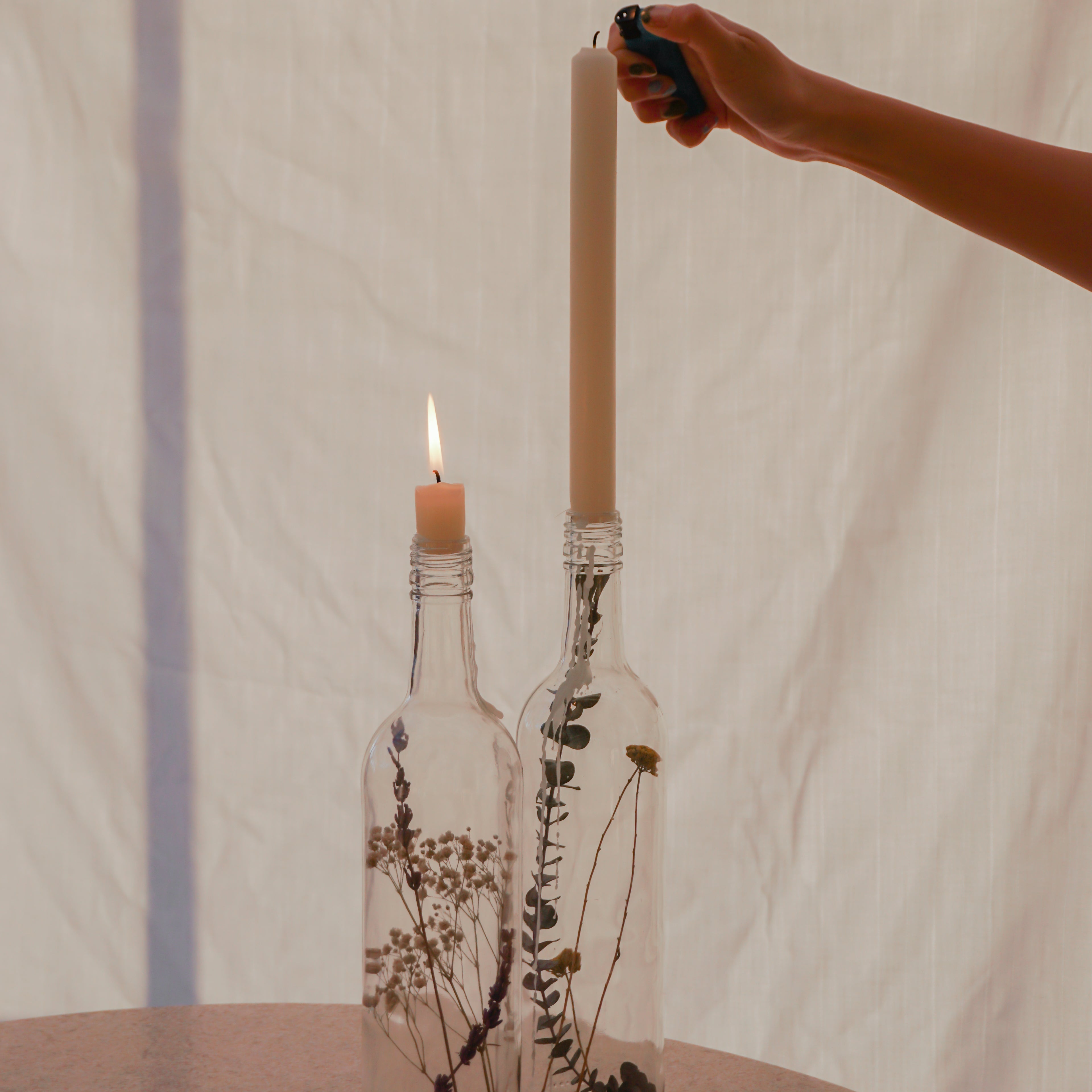 Detaljbild på två glasflaskor med torkade blommor och brinnande ljus i flaskhalsarna.