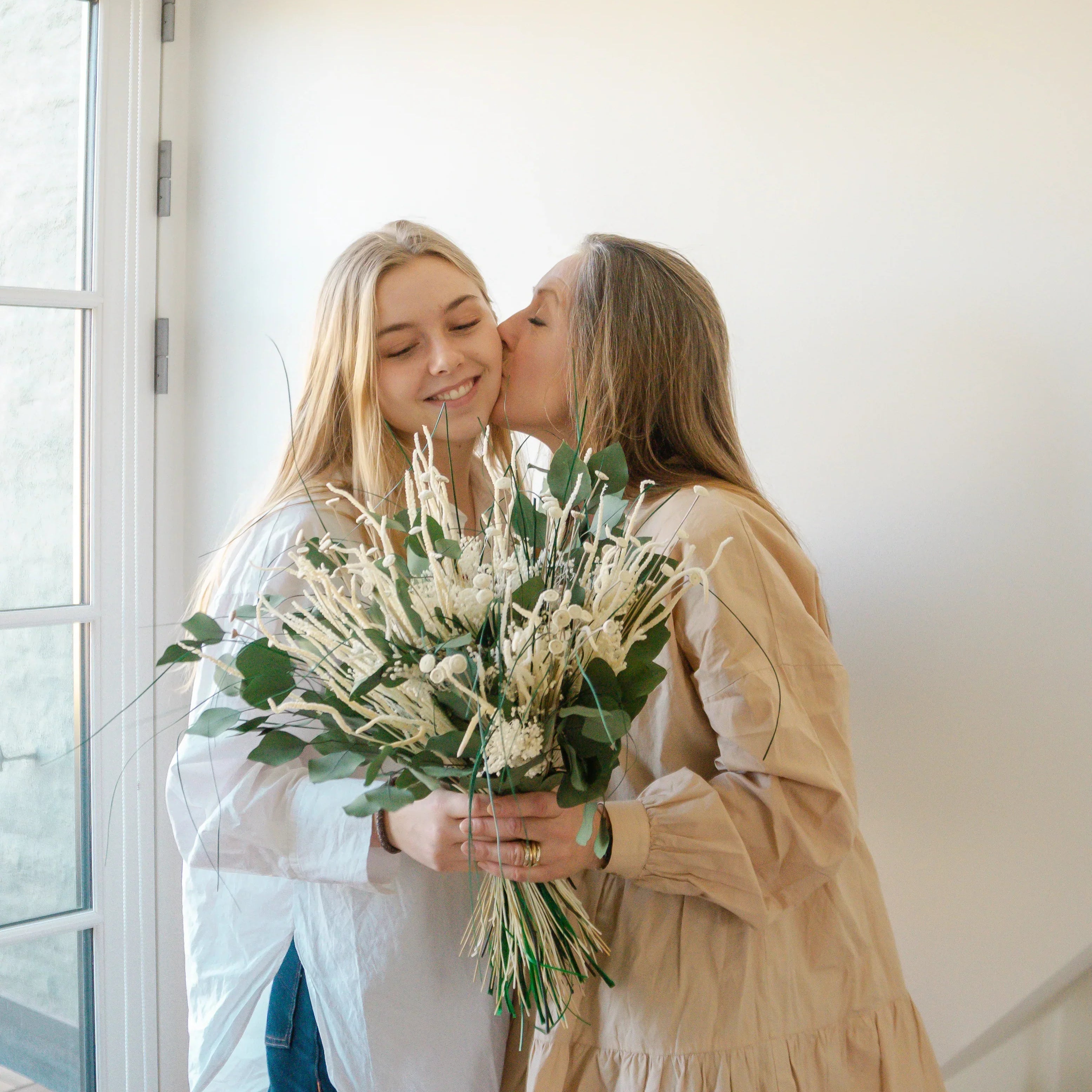 Kärleksfullt ögonblick på Mors dag – mamma pussar sin dotter och håller en vit-grön bukett.