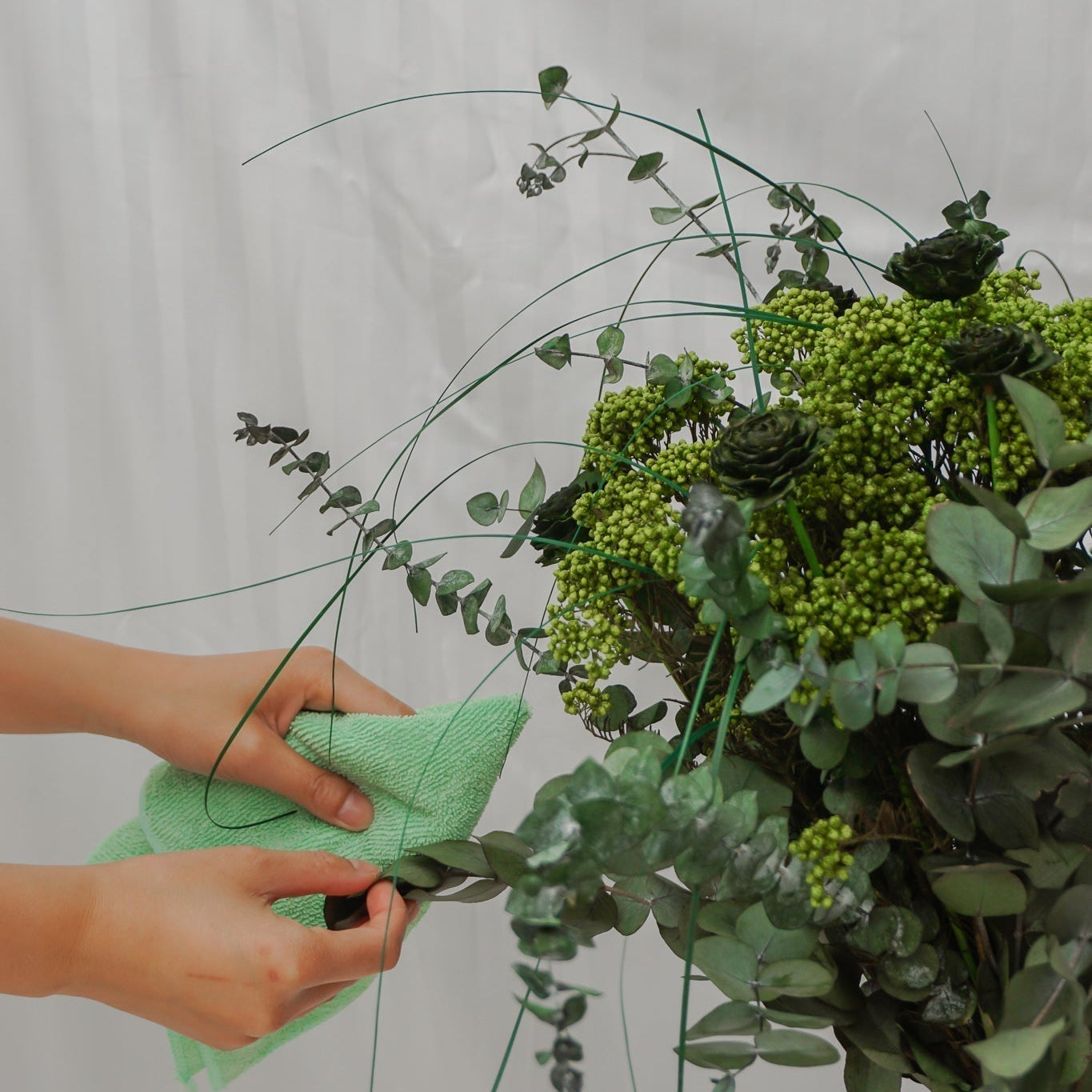 Närbild på någon som försiktigt dammar av blomsterbuketten Green Hope.