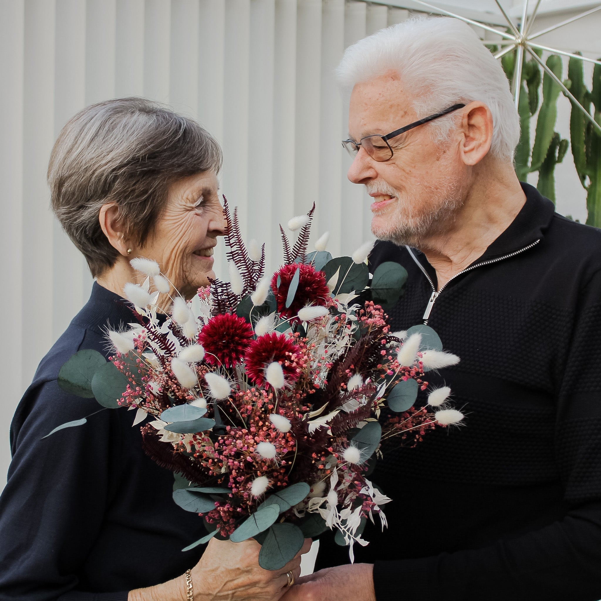 En leende man har överräckt en blombukett i vitt, rött och grönt till en glad kvinna.