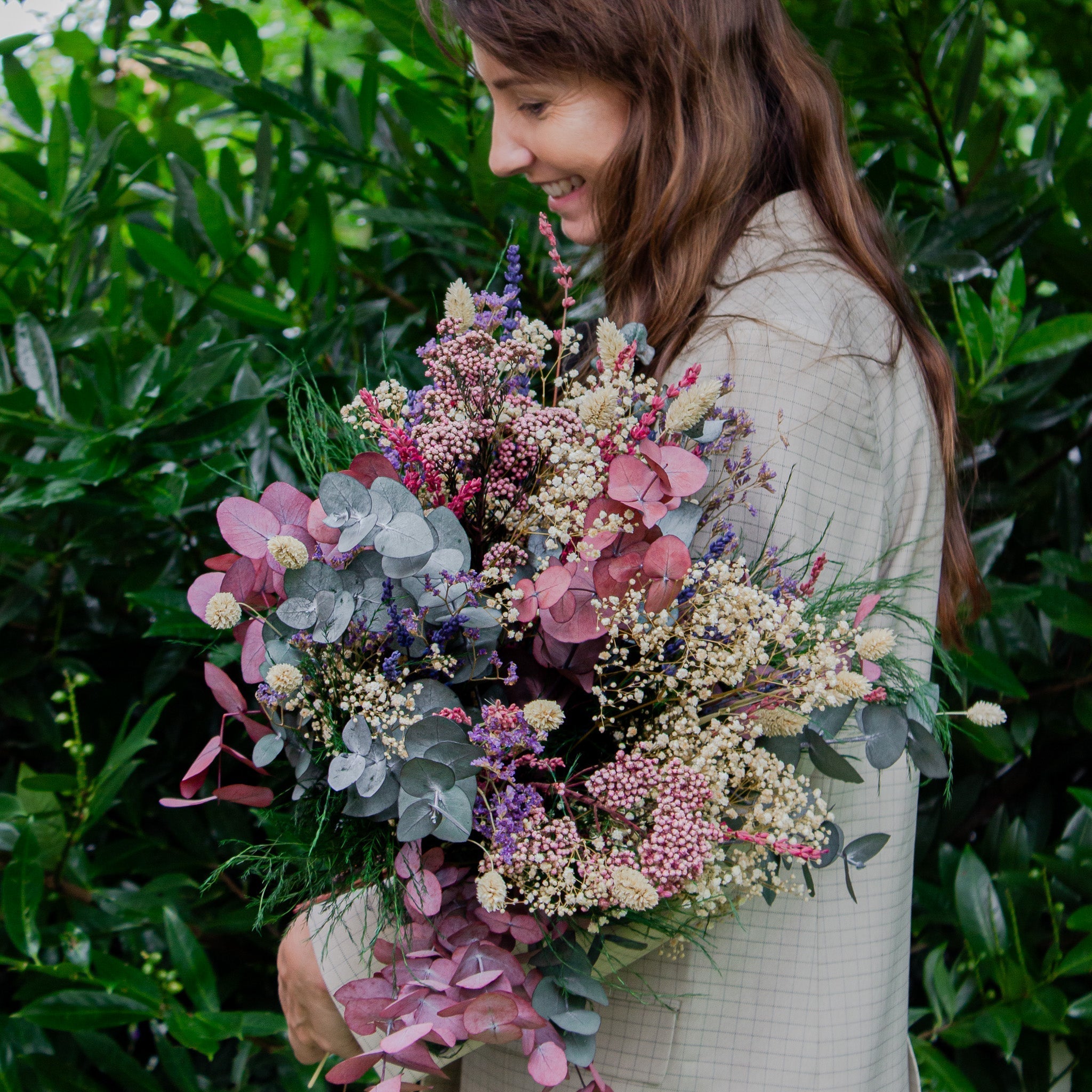 Kvinna sedd från sidan med en bukett innehållande eucalyptus och brudslöja i rosa och grönt.