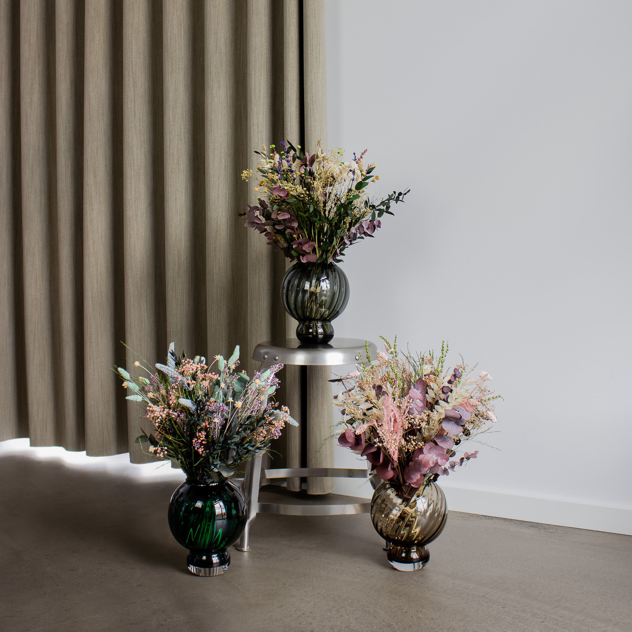 Tre blombuketter i olika nyanser varav den mittersta buketten står på en piedestal.