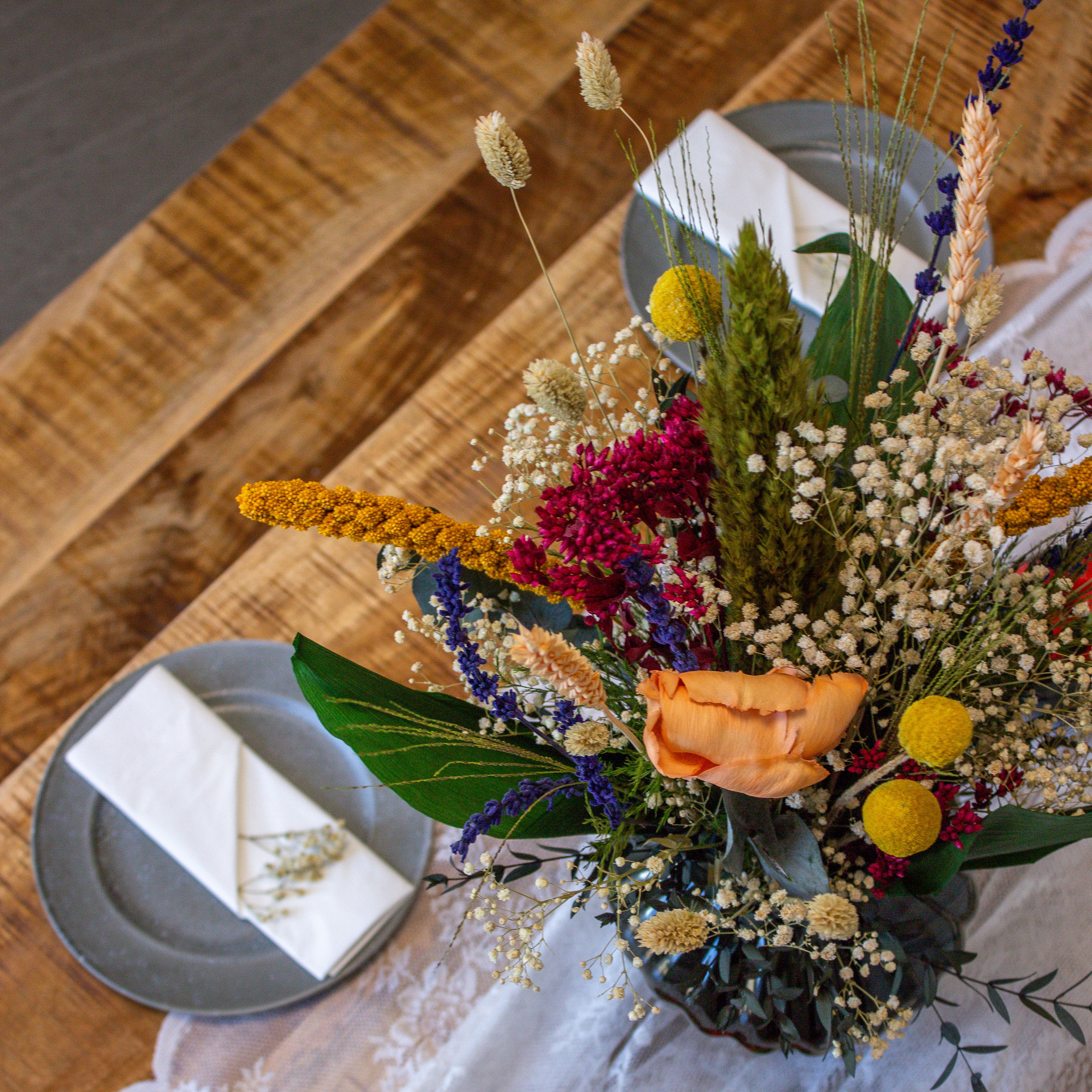 Stämningsfull dukning med bukett i orange, grönt, vitt, rosa, gult och blått som mittpunkt.