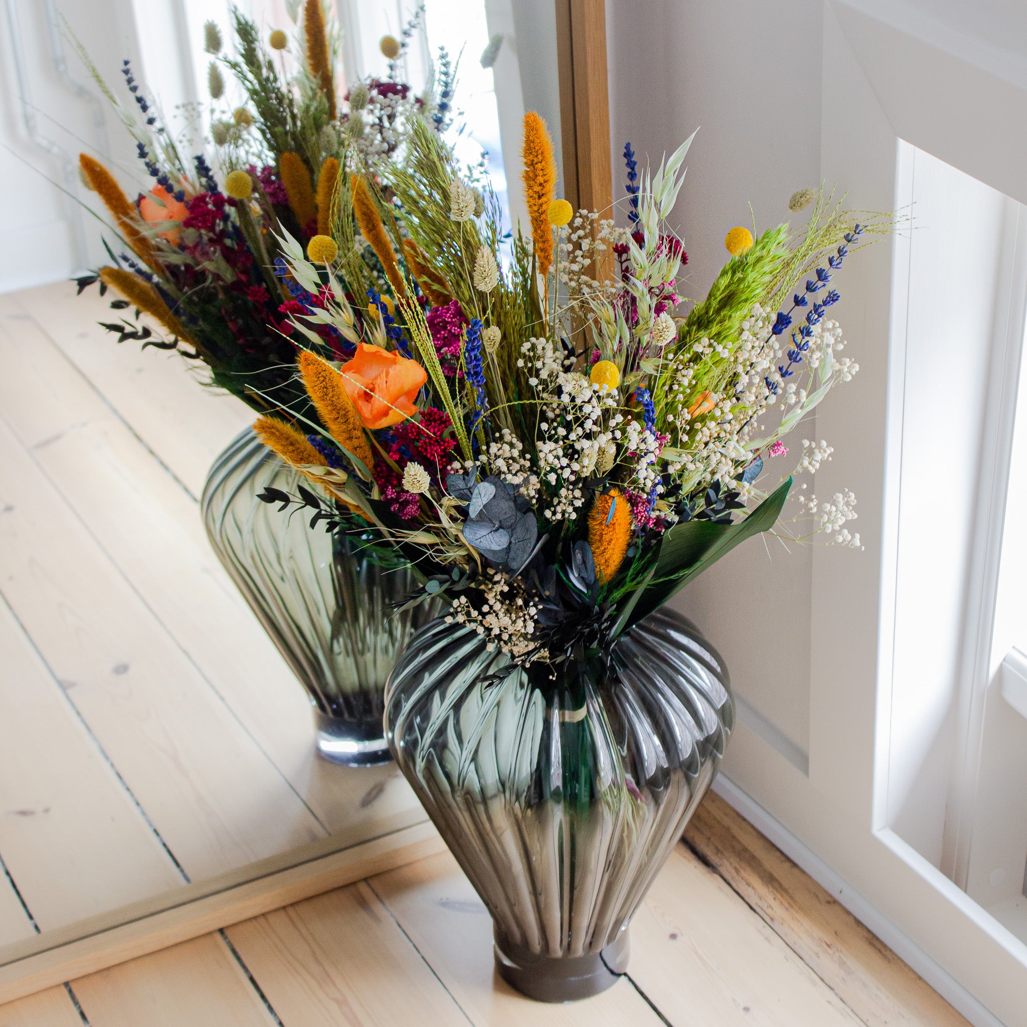 Vacker färgglad blombukett i regnbågens alla färger placerad i en glasvas framför en spegel.