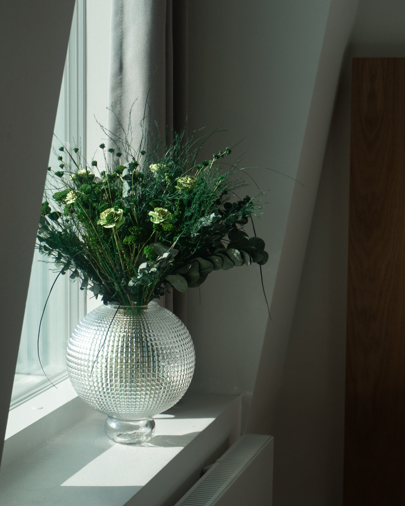 Grön bukett i en runt glasvas placerad på fönsterbrädan