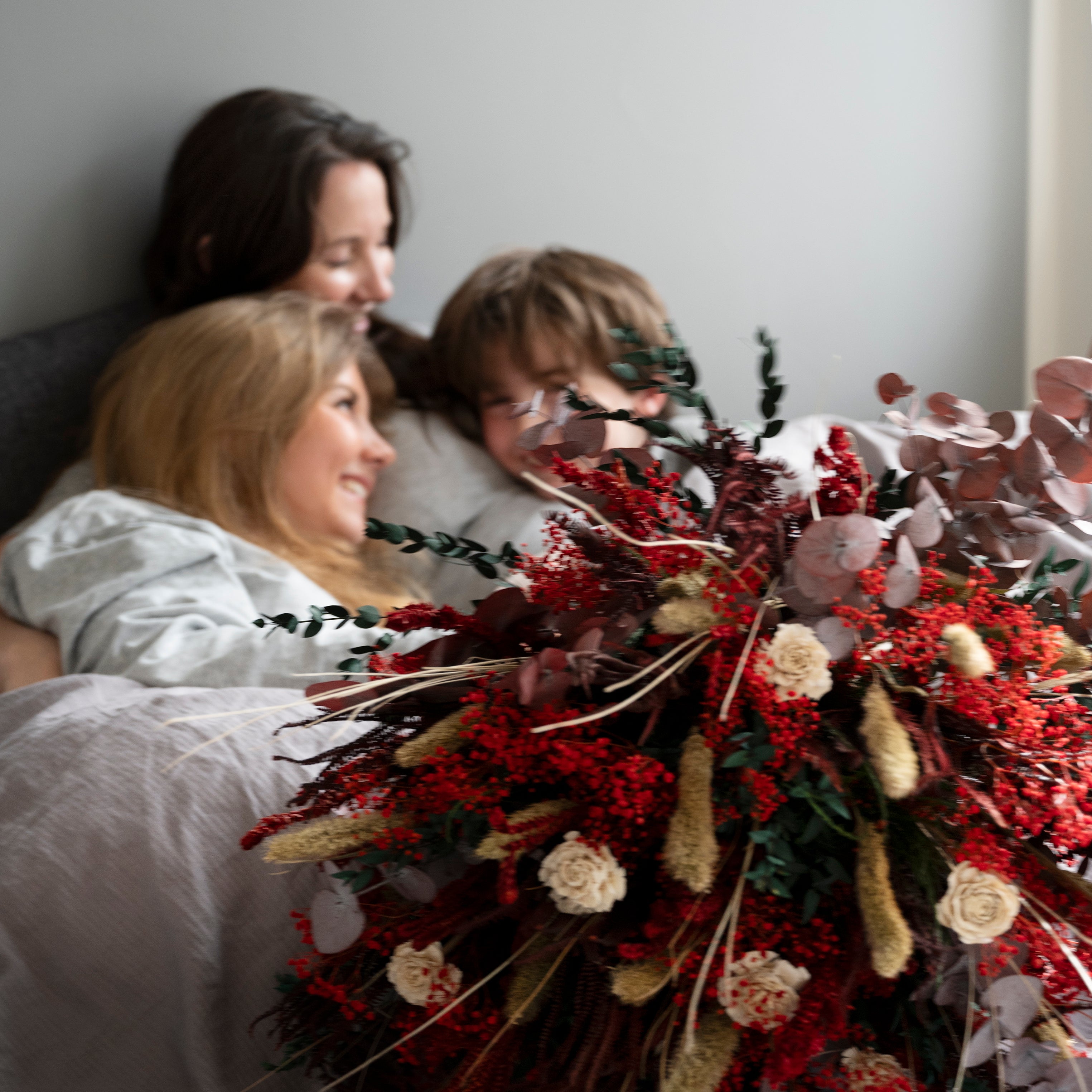 Barnen omfamnar sin mamma i sängen på mors dag efter att ha överraskat henne med en blombukett