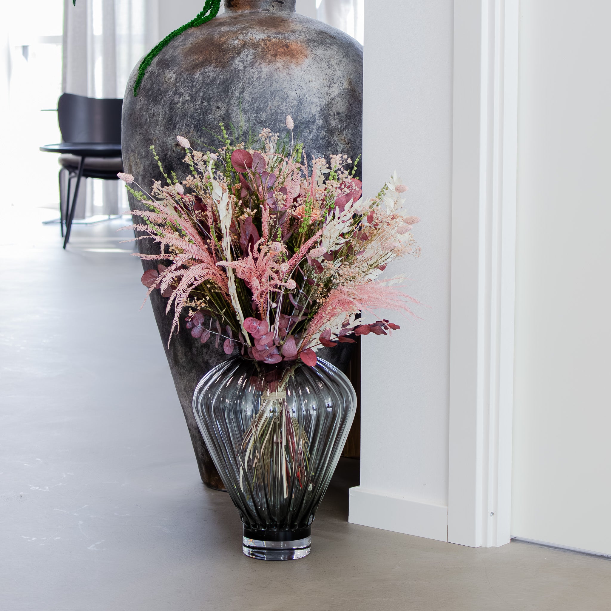 Rosa och grön bukett som står på golvet i en fin, grå glasvas.