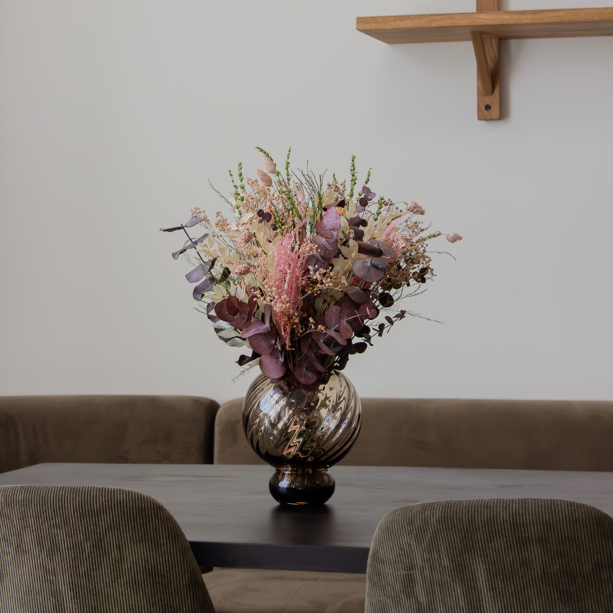 Bukett i dova, rosa och gröna färger i glasvas som pryder ett köksbord