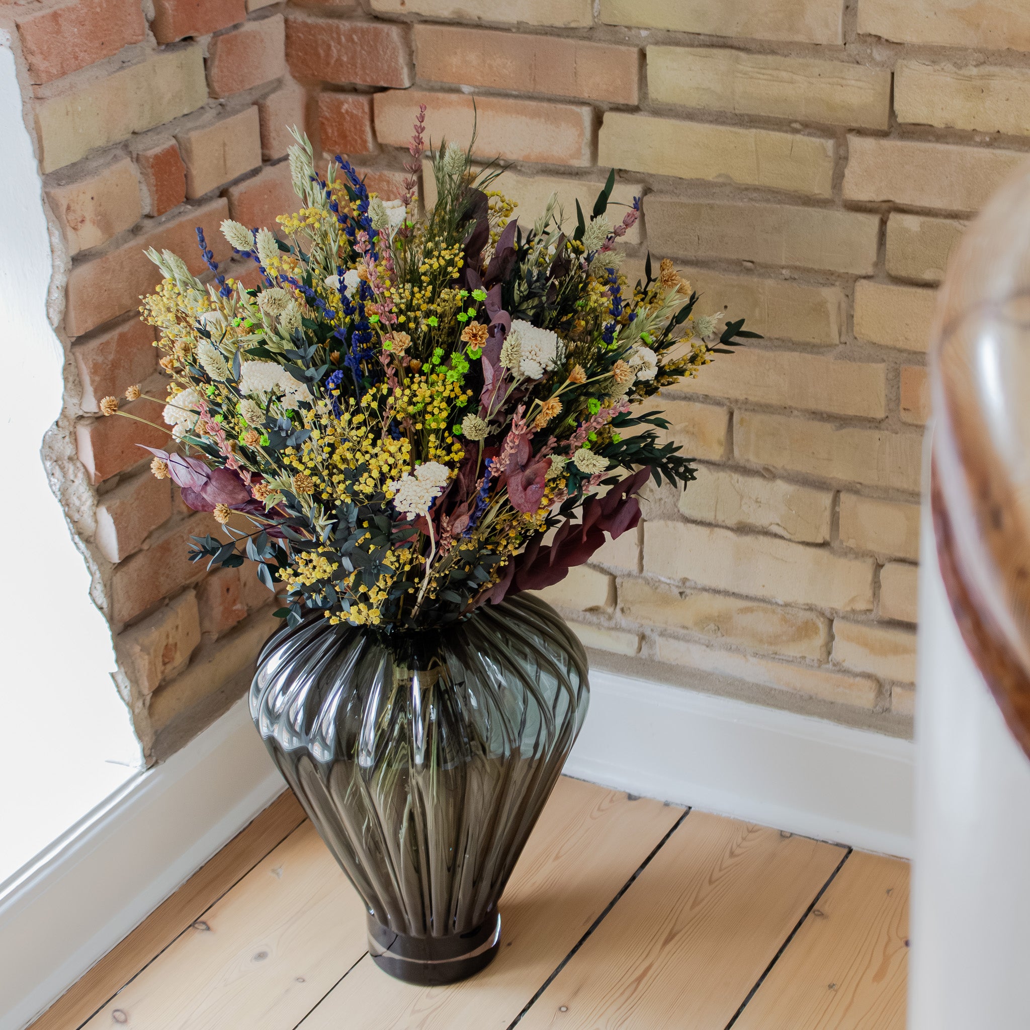 En färgglad bukett med vita, gröna, orangea, blåa blommor i glasvas på ett rustikt trägolv