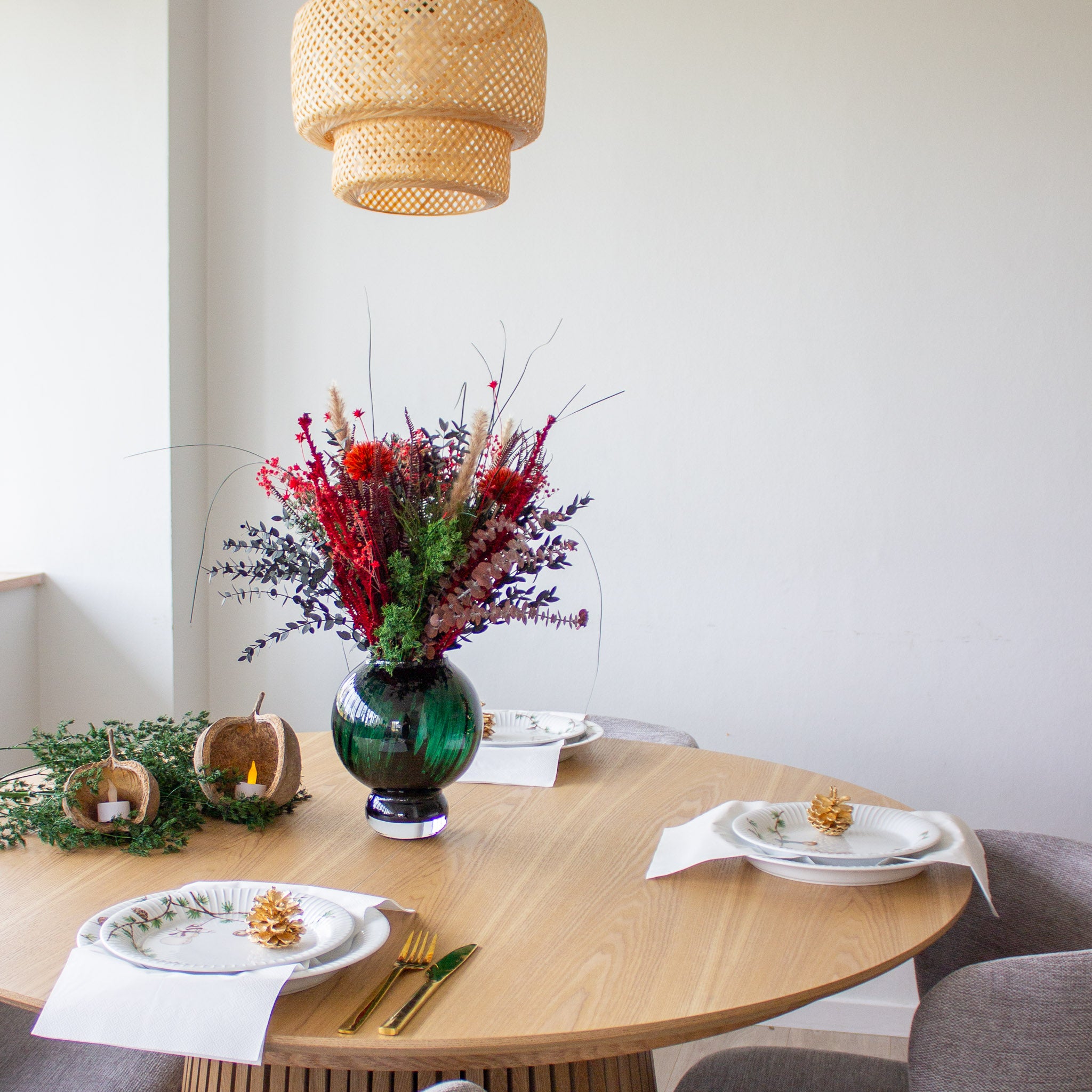 Julig dukning vid ett runt träbord där en rödgrön bukett står i mitten.
