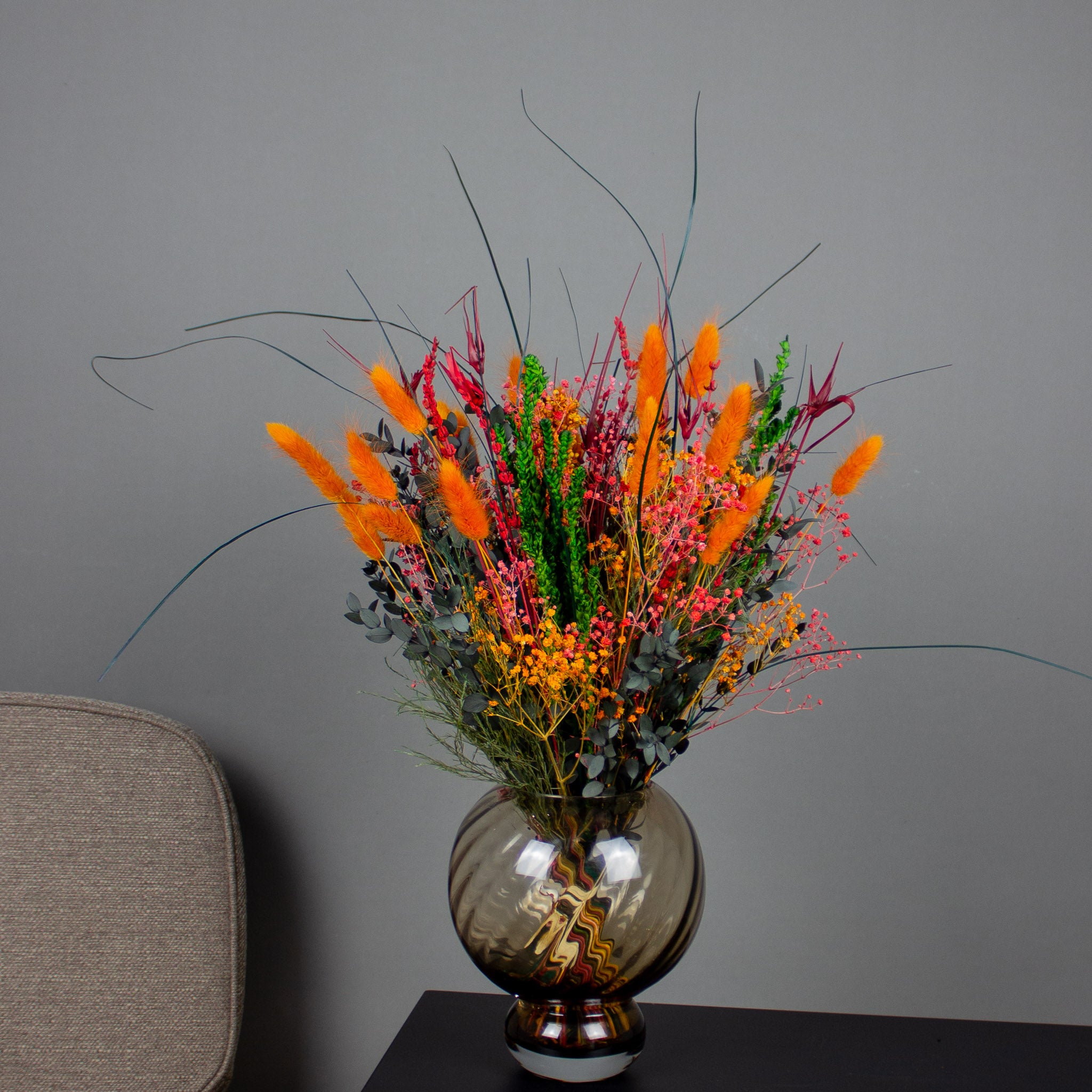 Orange Halloween-bukett i placerad i en brun glasvas på ett svart litet bord