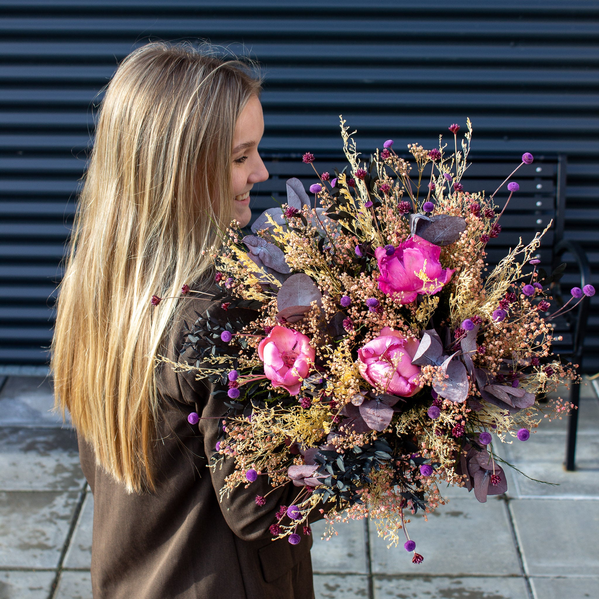 Ung kvinna håller en elegant bukett i rosa, lila, gröna och beige nyanser.