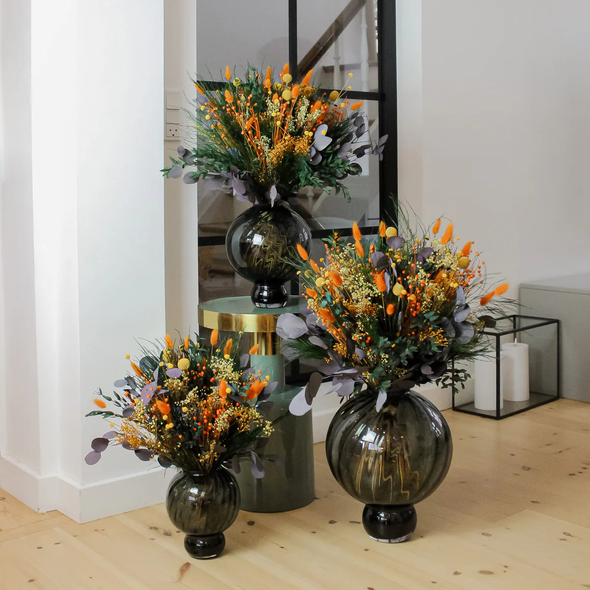 Tre vackra orangea buketter i tre storlekar, varav den ena står på en piedestal.