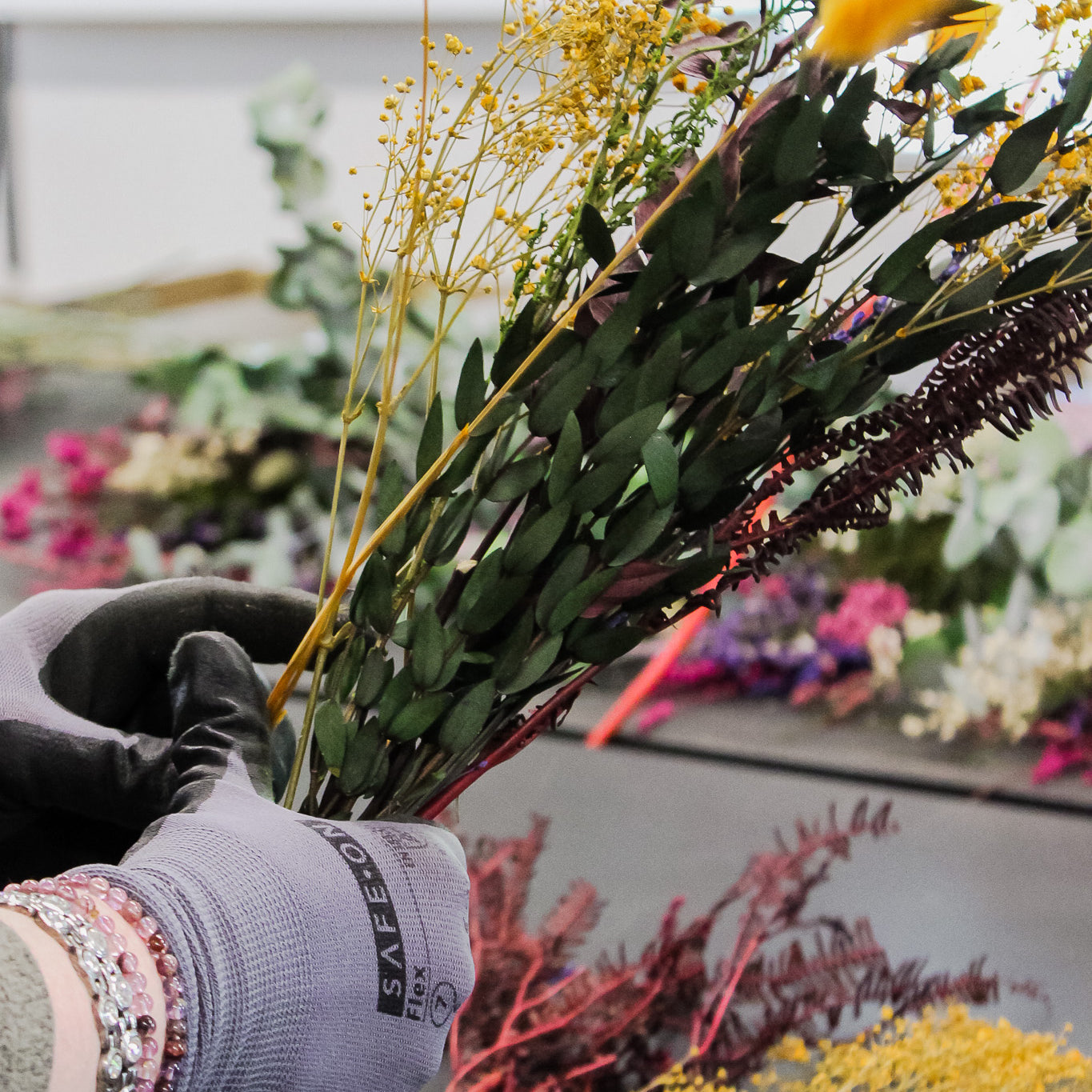 Närbild på händer med arbetshandskar som binder en bukett blommor.