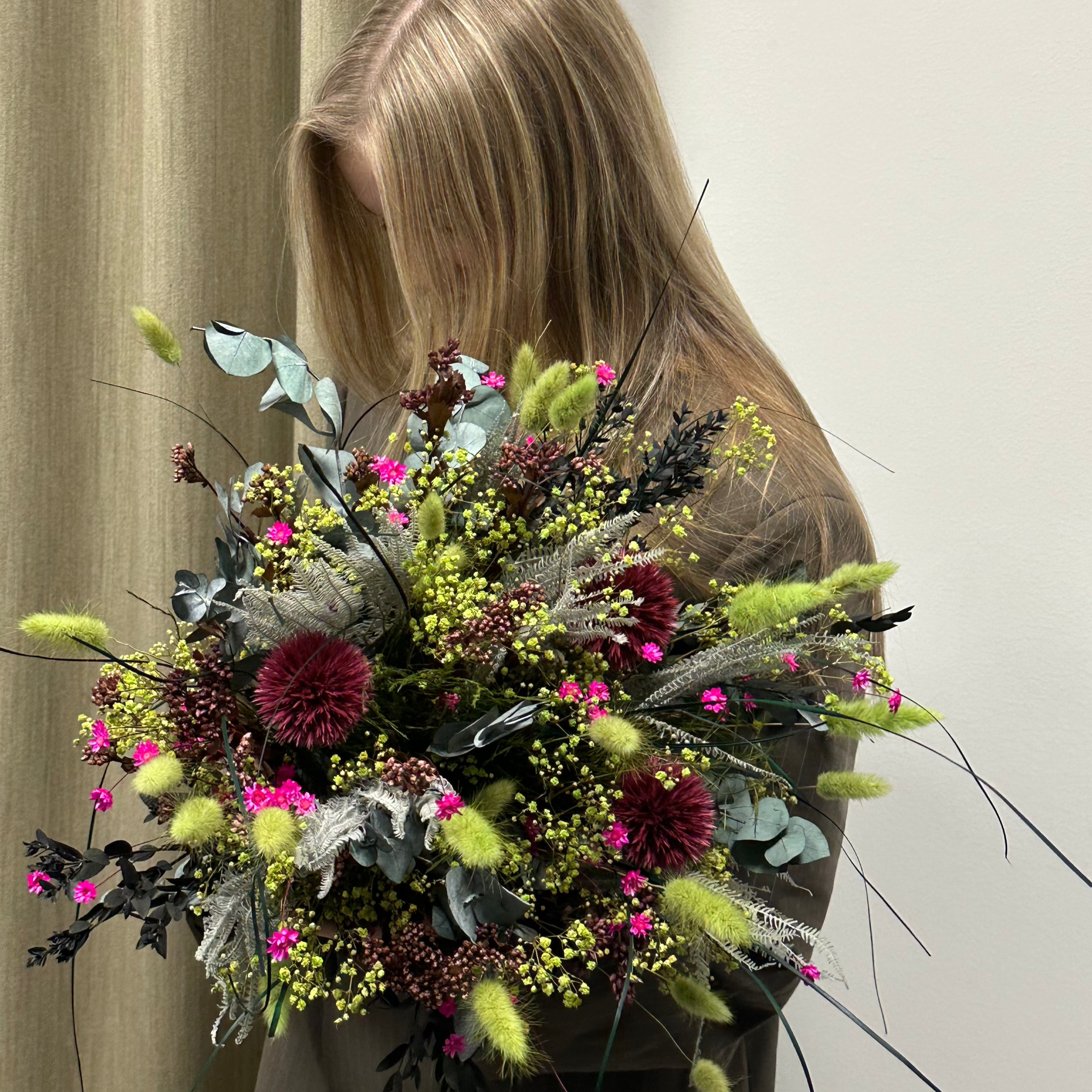Kvinna håller i och tittar ner på en rosa och grön blombukett som vilar i hennes arm.