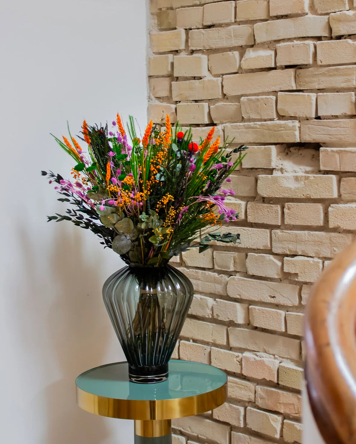 En färgsprakande bukett i lila, grönt och orange på en piedestal framför en tegelvägg