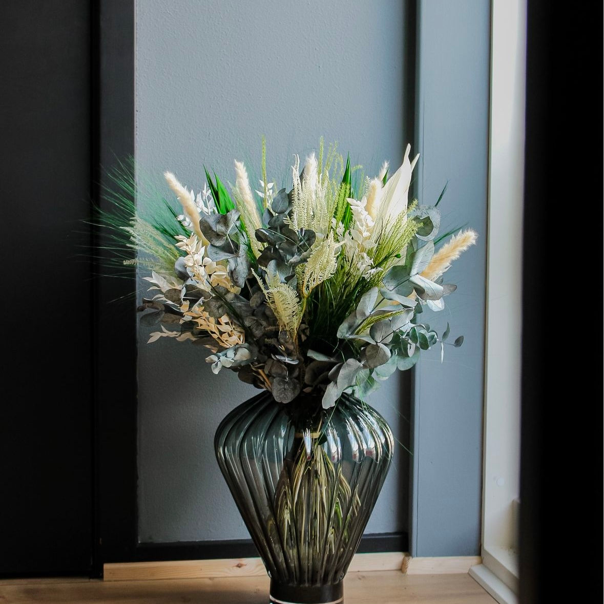 Bukett i gröna och vita nyanser placerad i en glasvis på ett golv