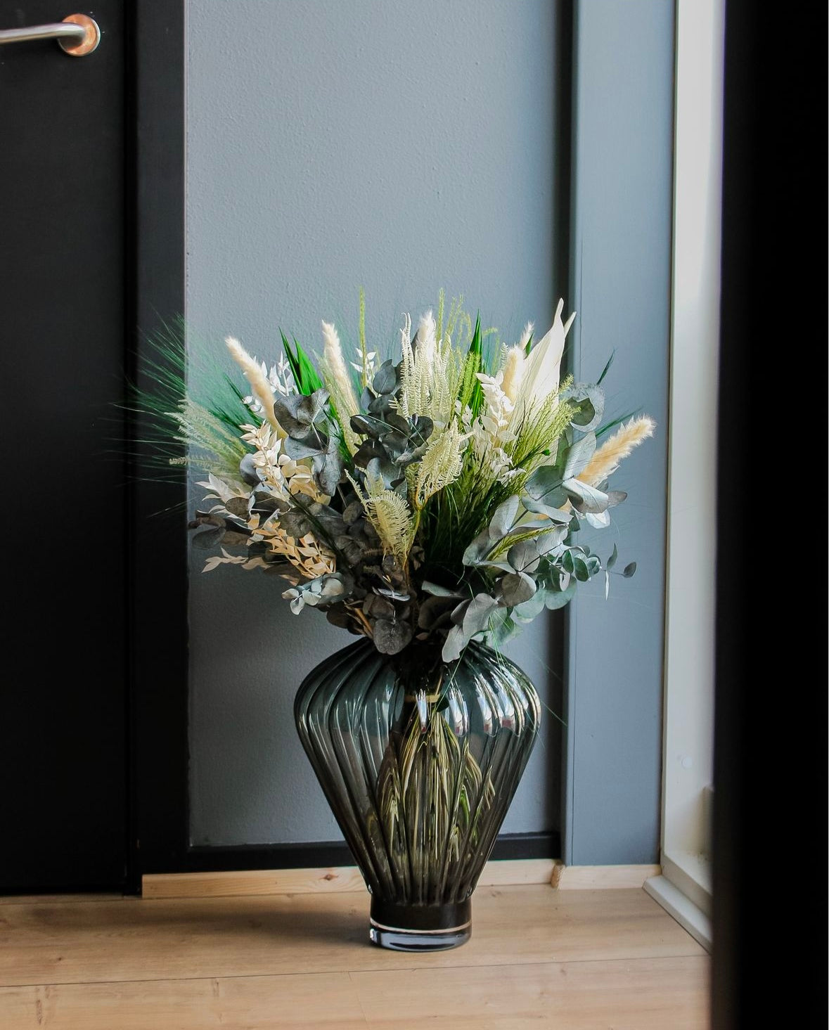 Bukett i gröna och vita nyanser placerad i en glasvis på ett golv