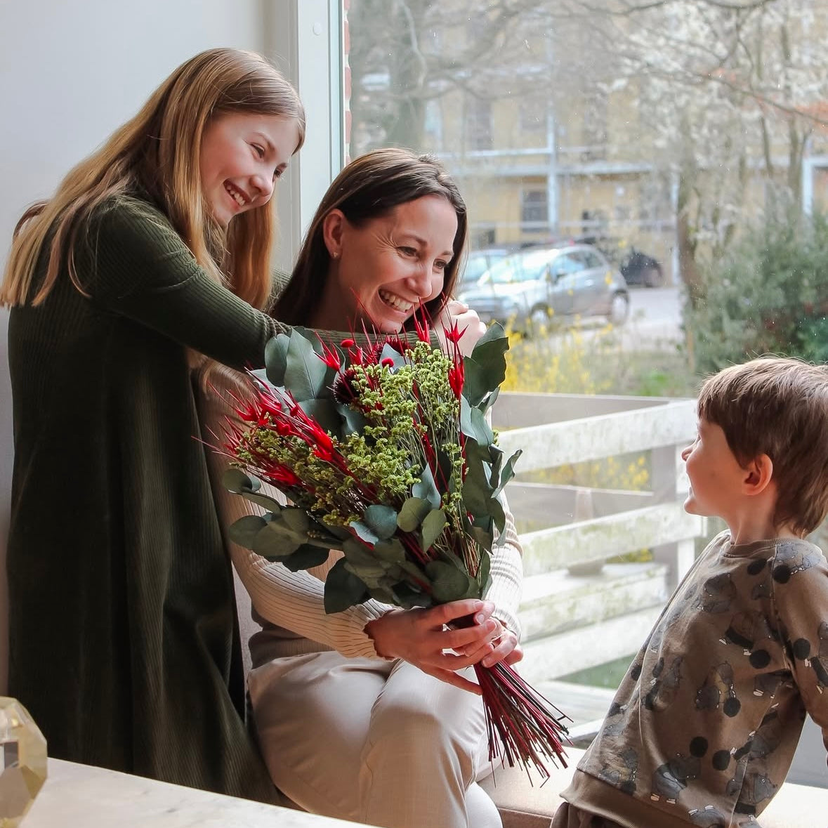 Mamma som håller en blombukett omringad av sina två barn