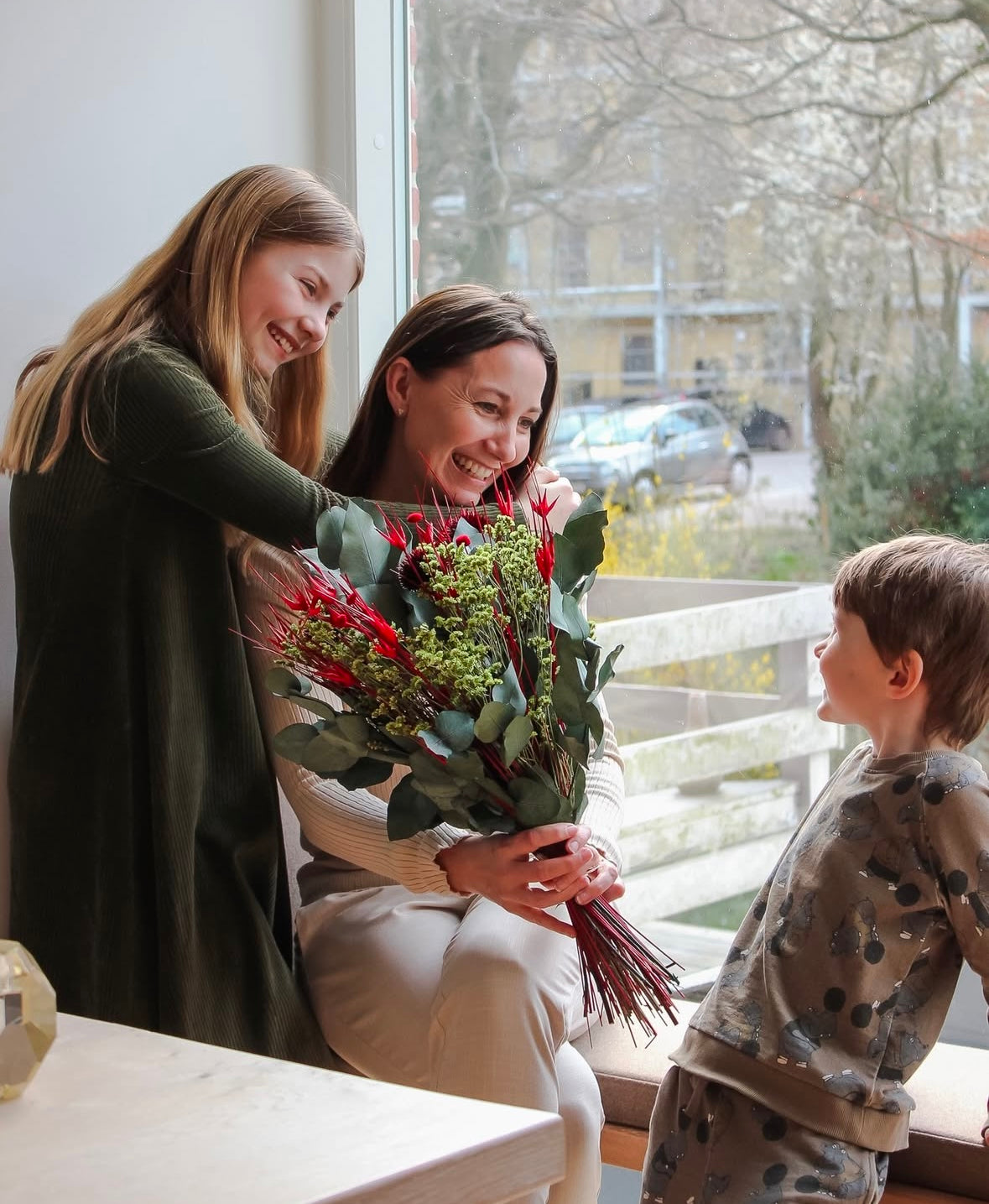 Mamma som håller en blombukett omringad av sina två barn