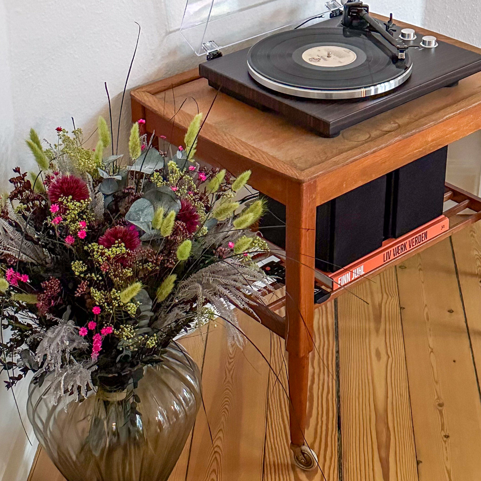 En bukett i rosa och grönt står bredvid en gammal LP-spelare på trägolv