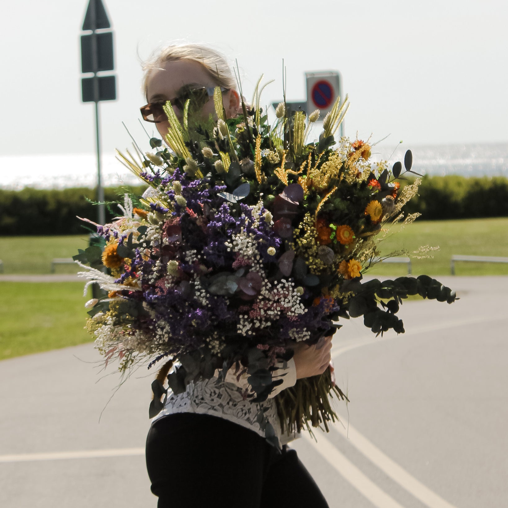 Utomhus bild av ung kvinna med solglasögon som håller fyra olika buketter tillsammans som en enda stor blombukett.