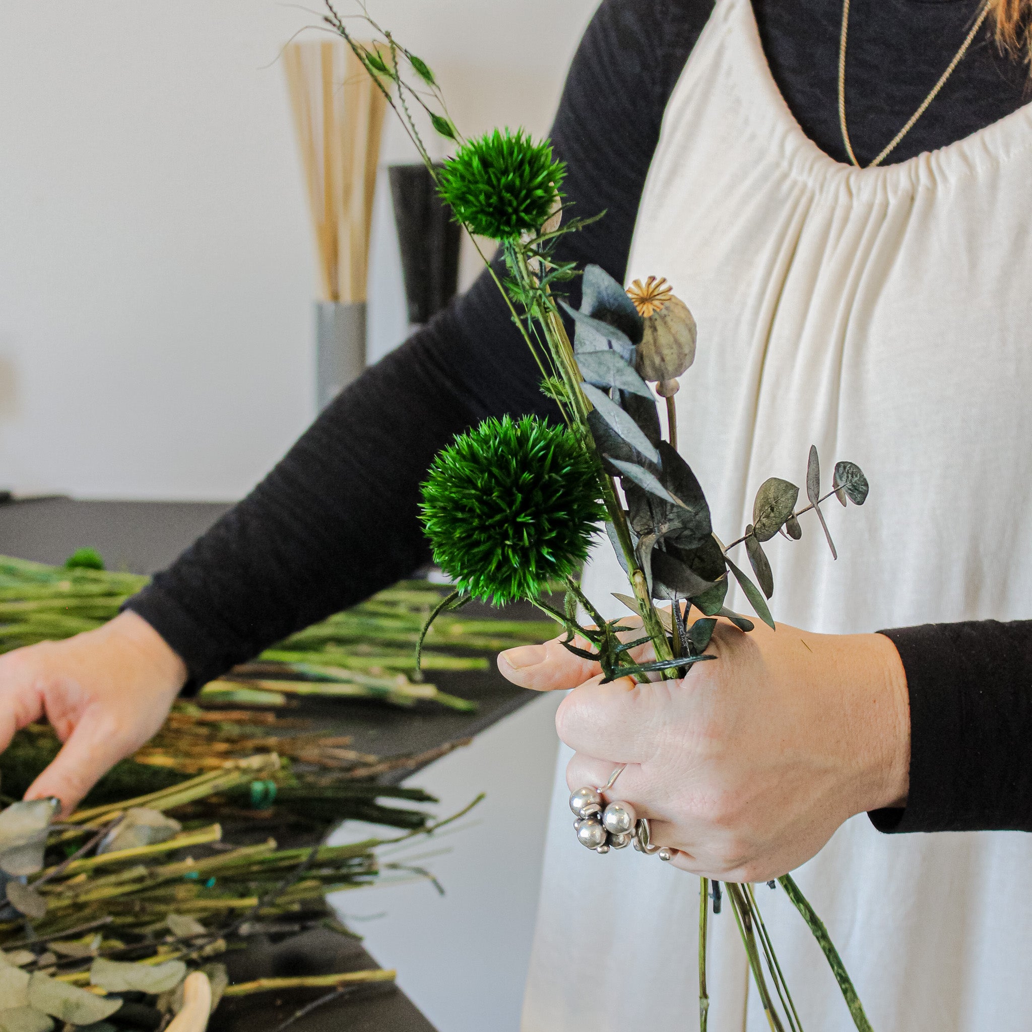 Kvinna som binder en grön blombukett med b.la eucalyptus och tistel