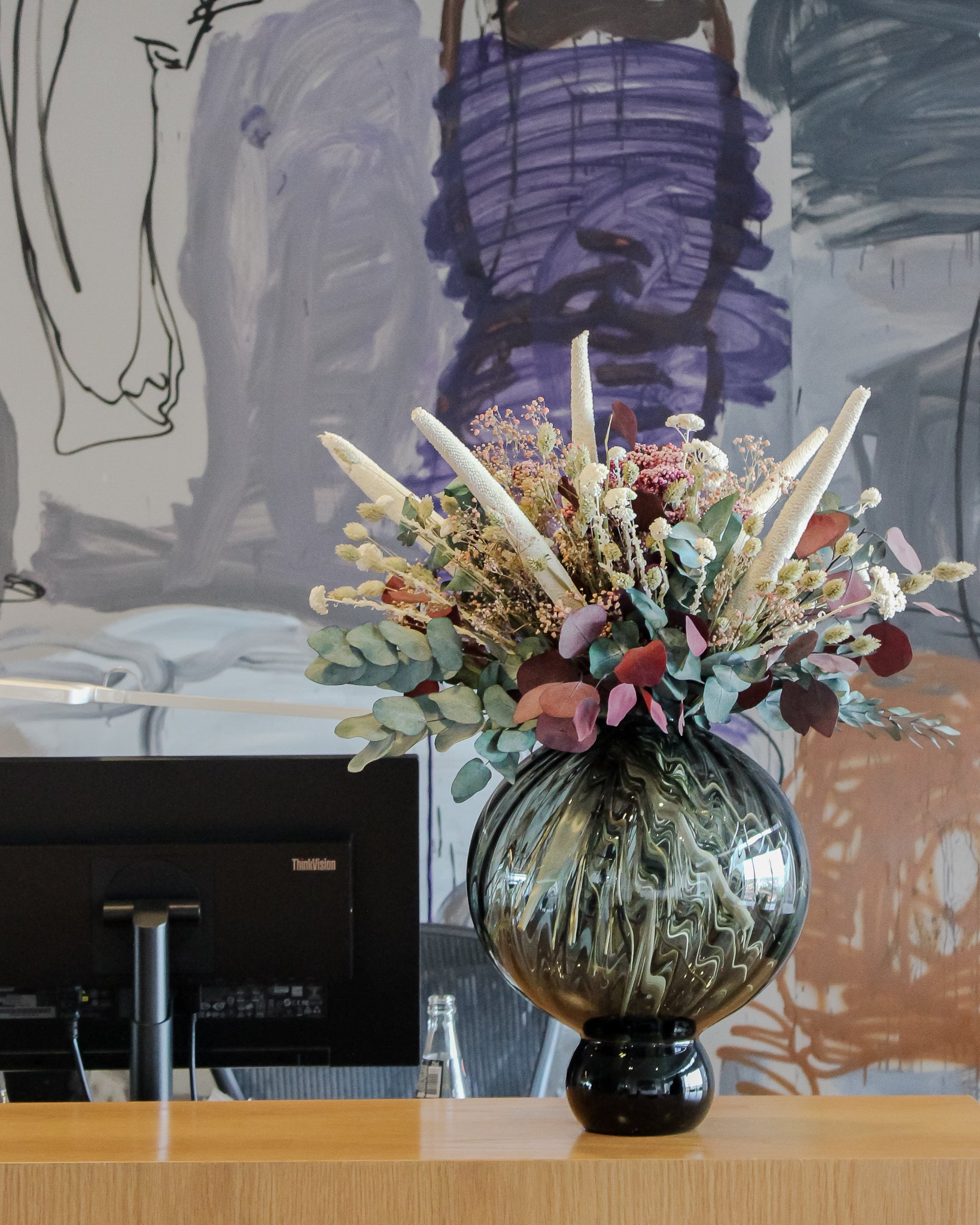 Vacker blombukett i vitt, grönt och rosa pryder en recentionsisk med en dator och en stor tavla i bakgrunden.