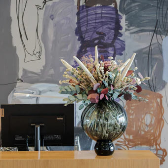 Pampig bukett i vitt, rosa och grönt står på en receptionsdisk