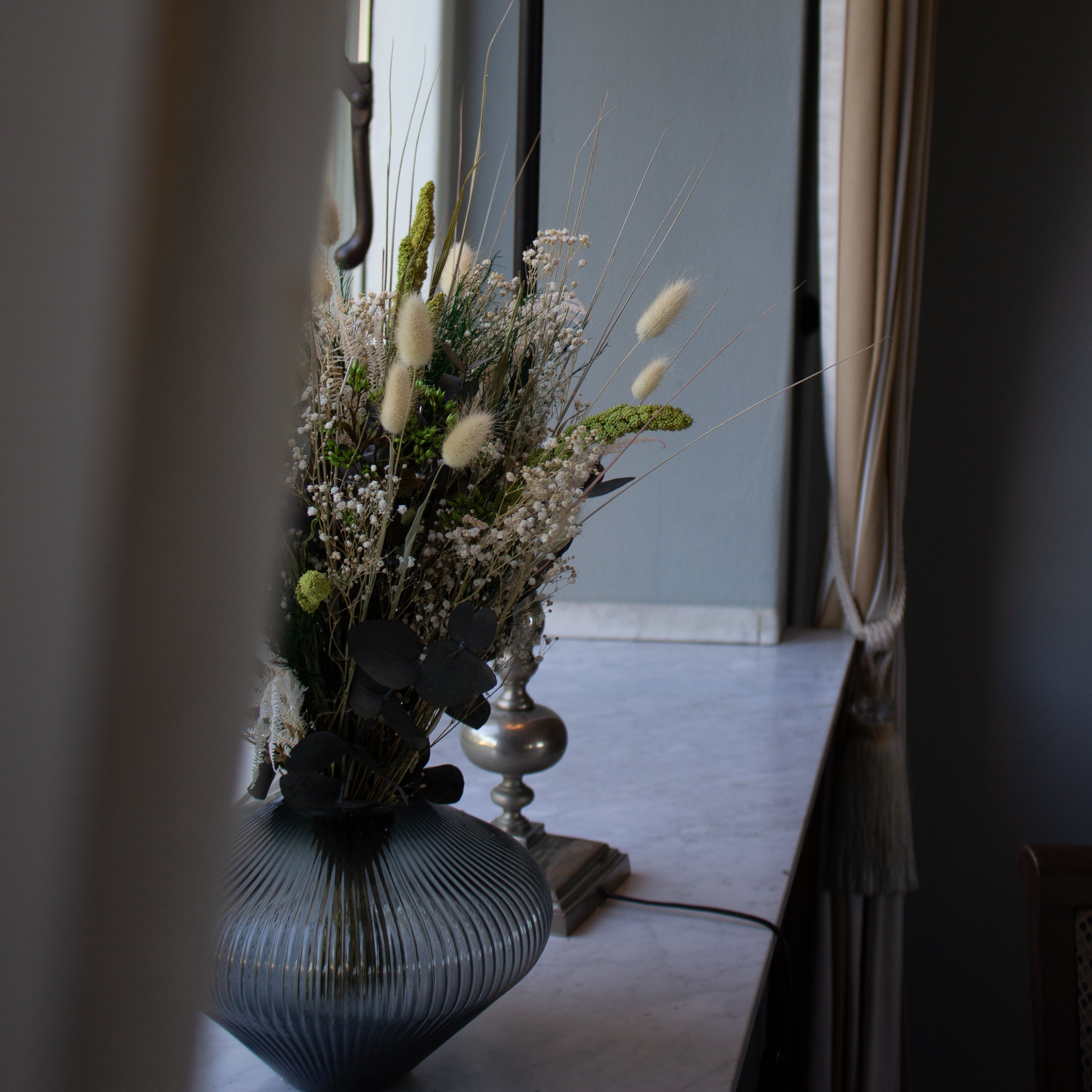 Bukett Grön Harmoni med gröna och vita nyanser placerad i en glasvas på en fönsterbräda av marmor