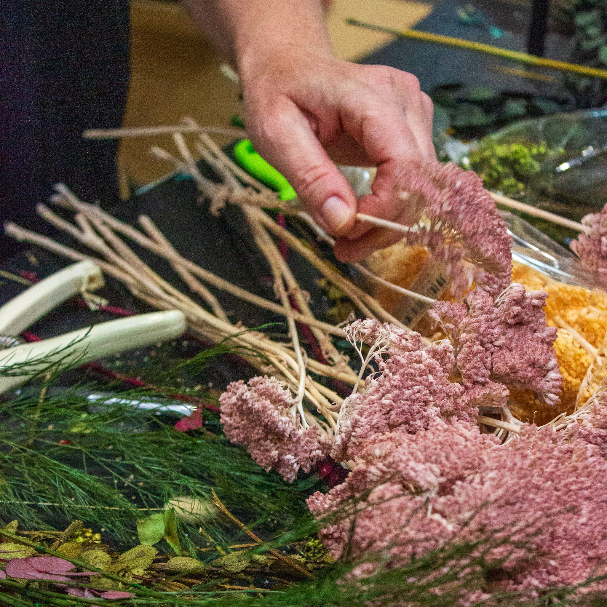 Närbild av en hand som tar upp en rosa blomma från arbetsbordet