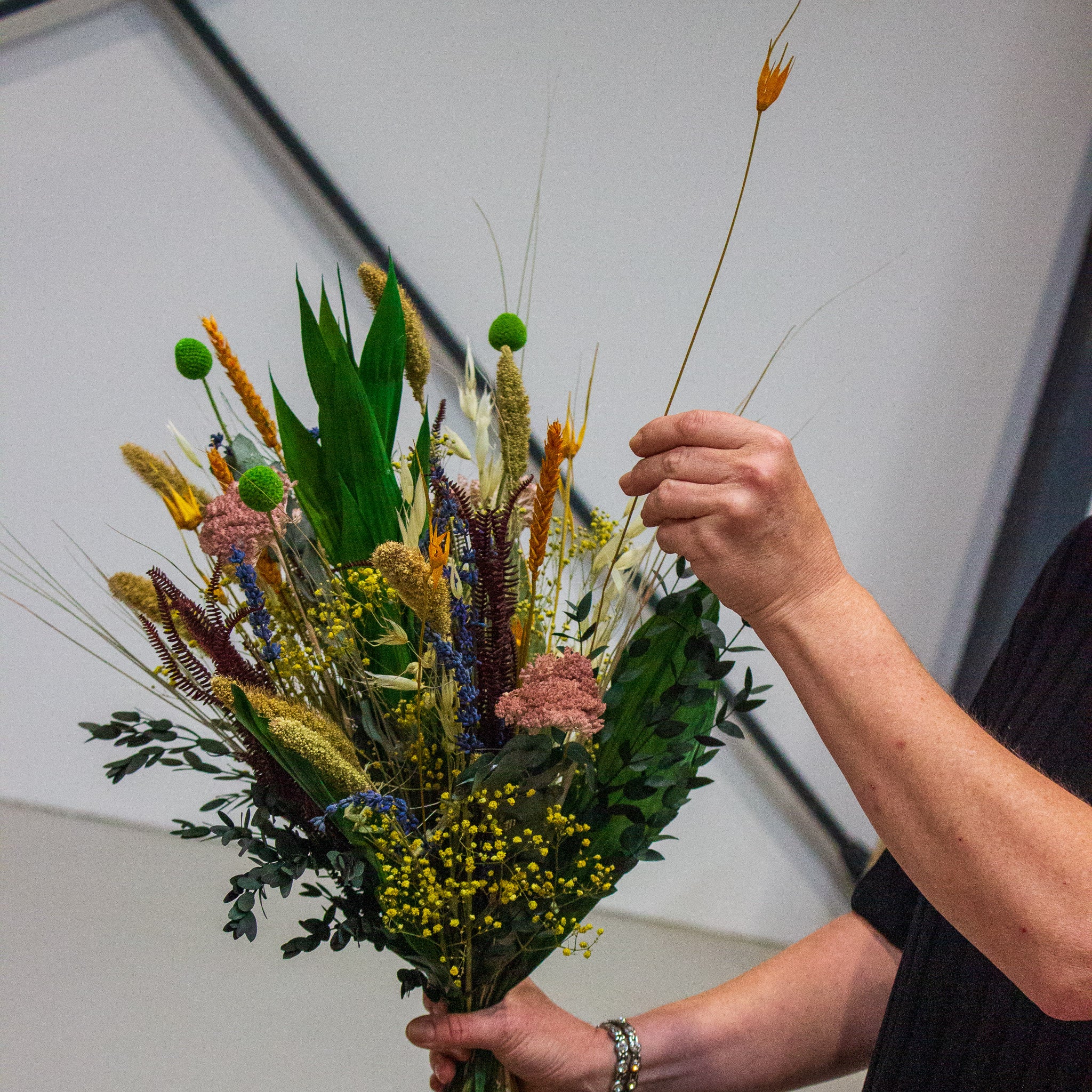 Närbild av händer som binder en blombukett i gula, gröna och orange nyanser