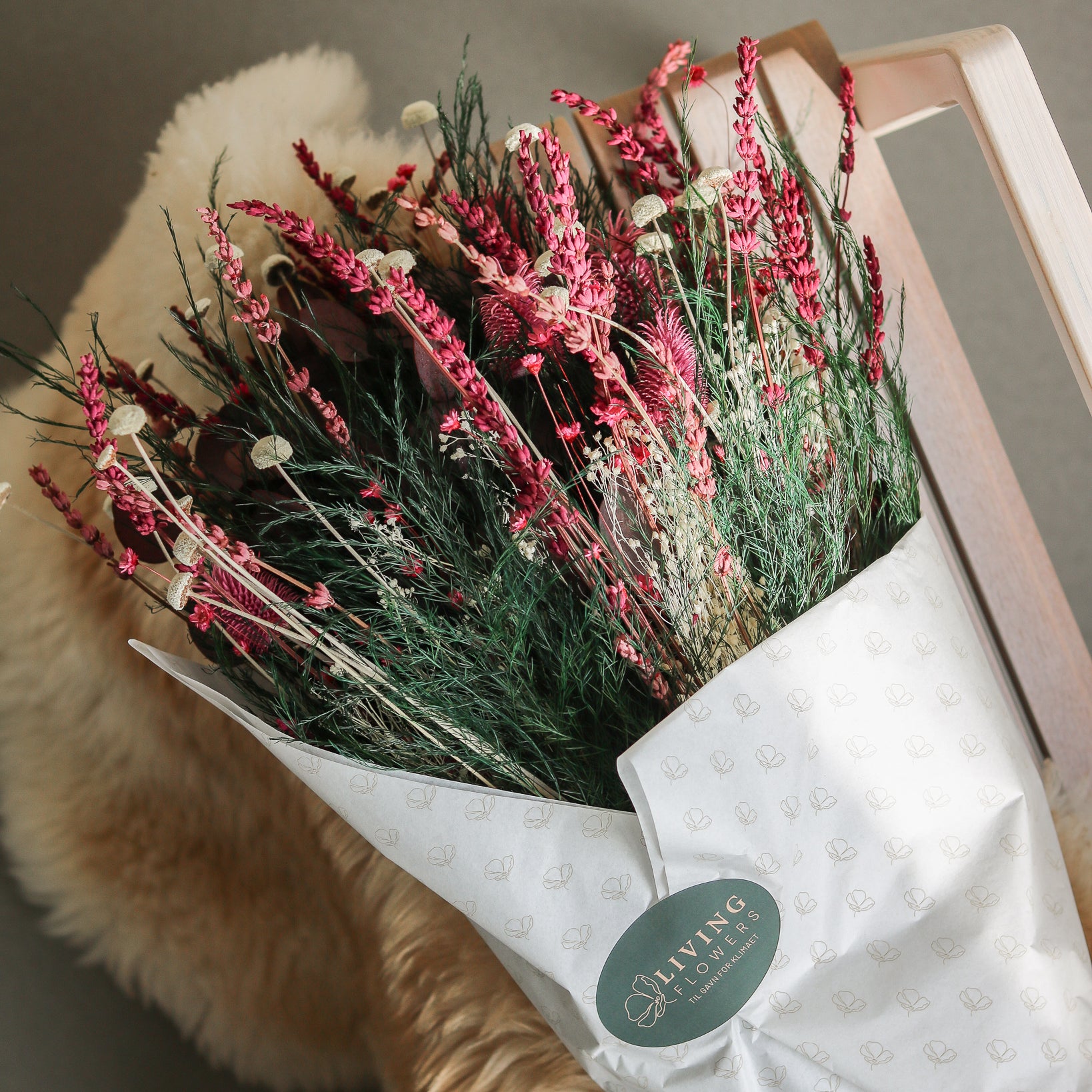 Bukett i rött och grönt vackert inslagen i vitt silkespapper står på en stol i trä