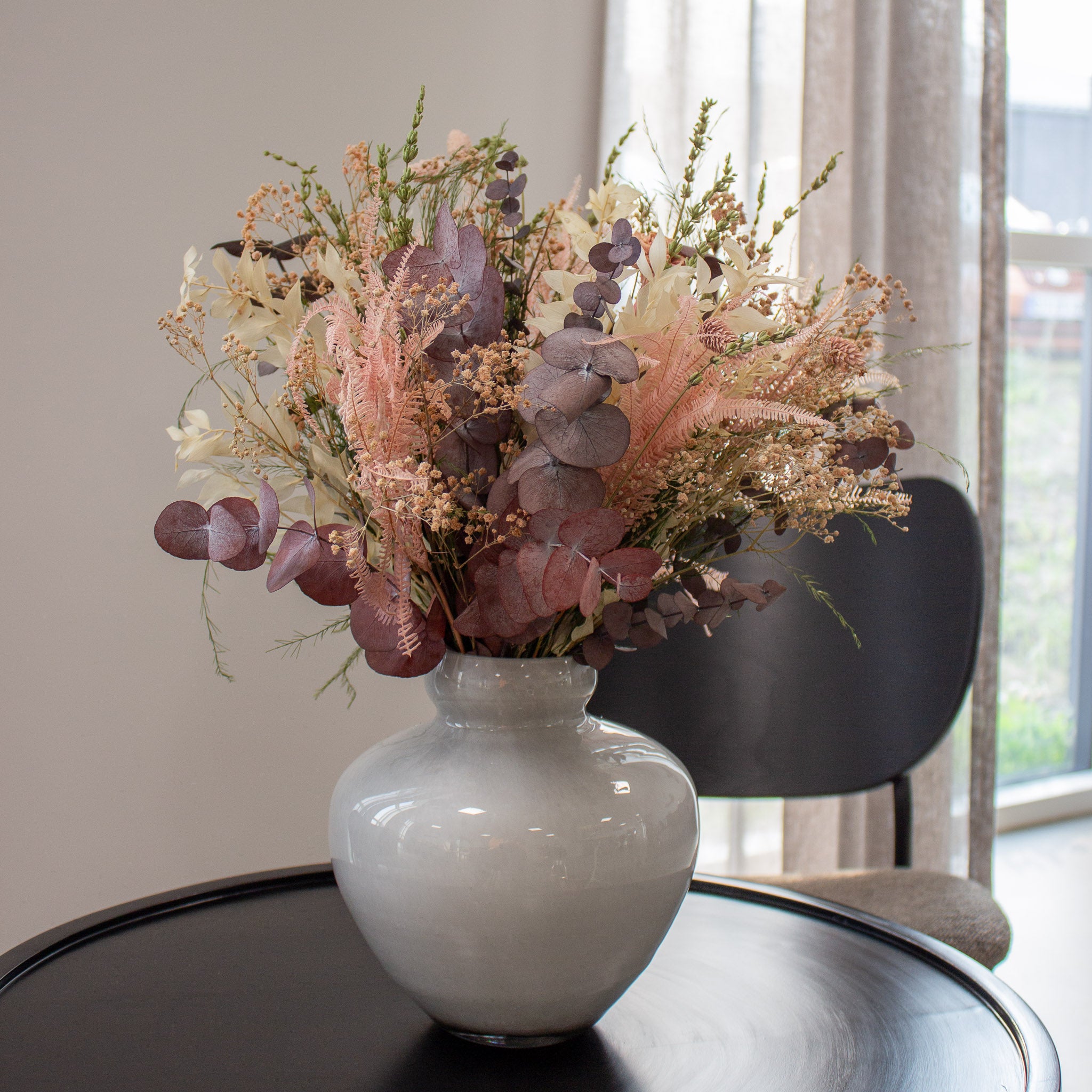 En vit dekorativ glasvas med en rosa bukett lacerad på ett litet runt bord.