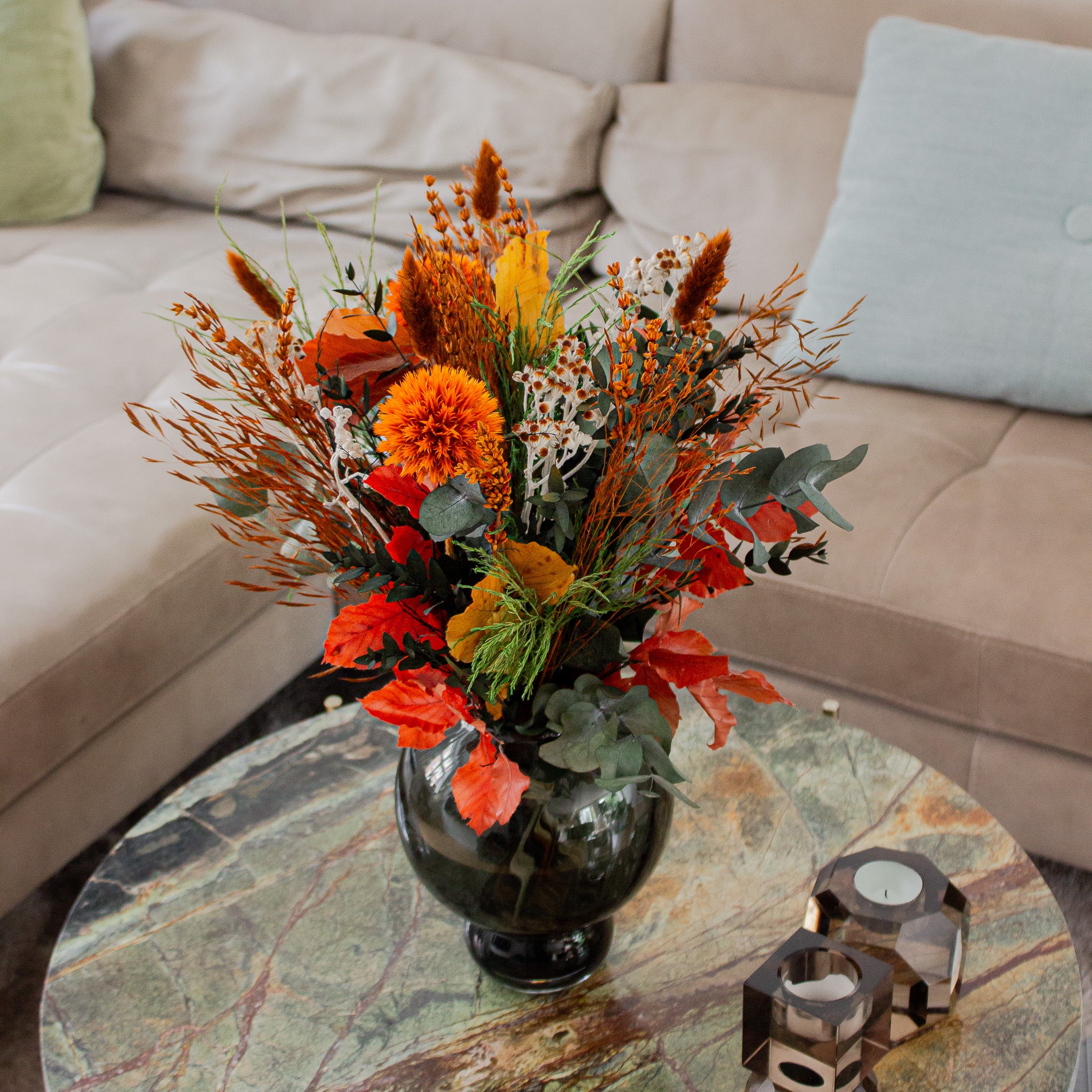 Vacker orange bukett placerad på ett brunt marmorbord bredvid en rosa soffa.