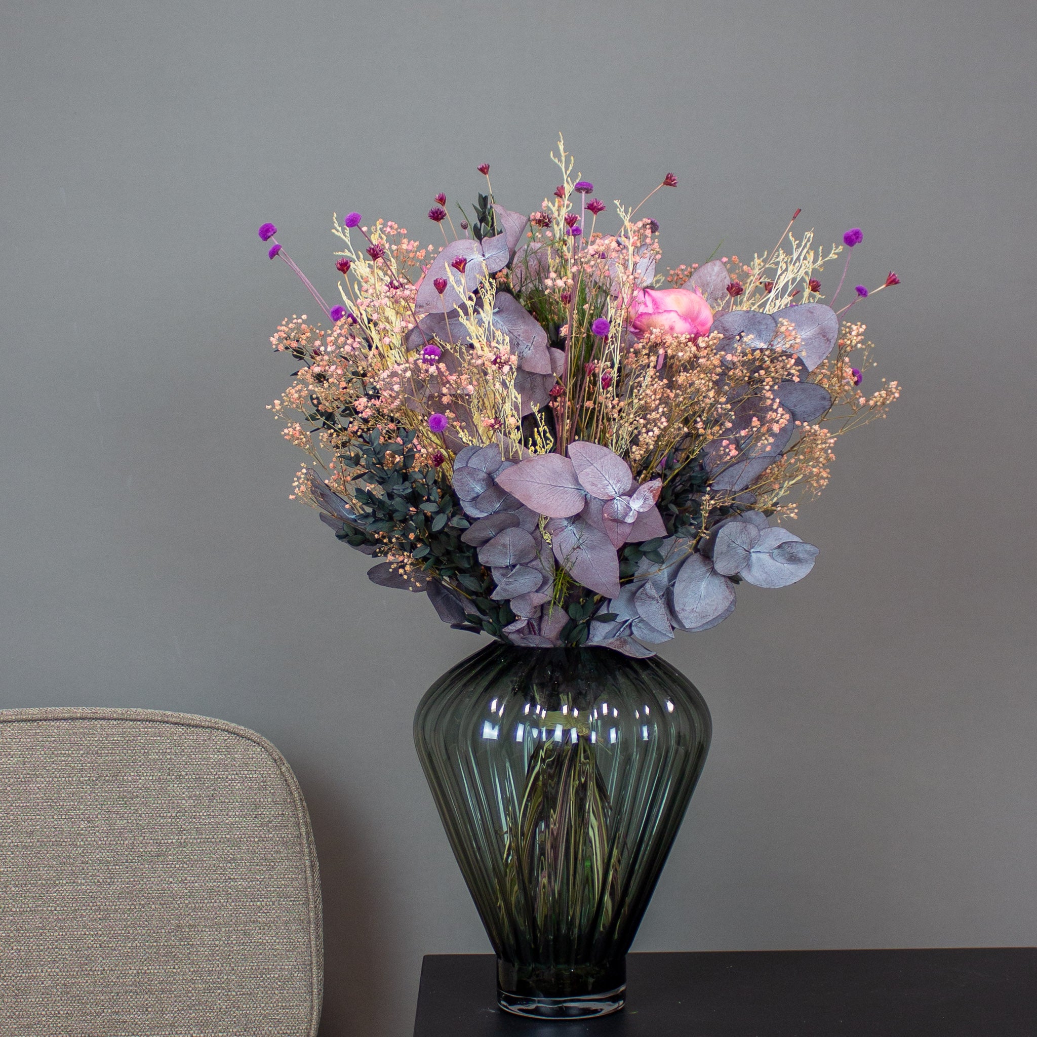 Vacker bukett i rosa, lila och beige placerad i en grön glasvas.