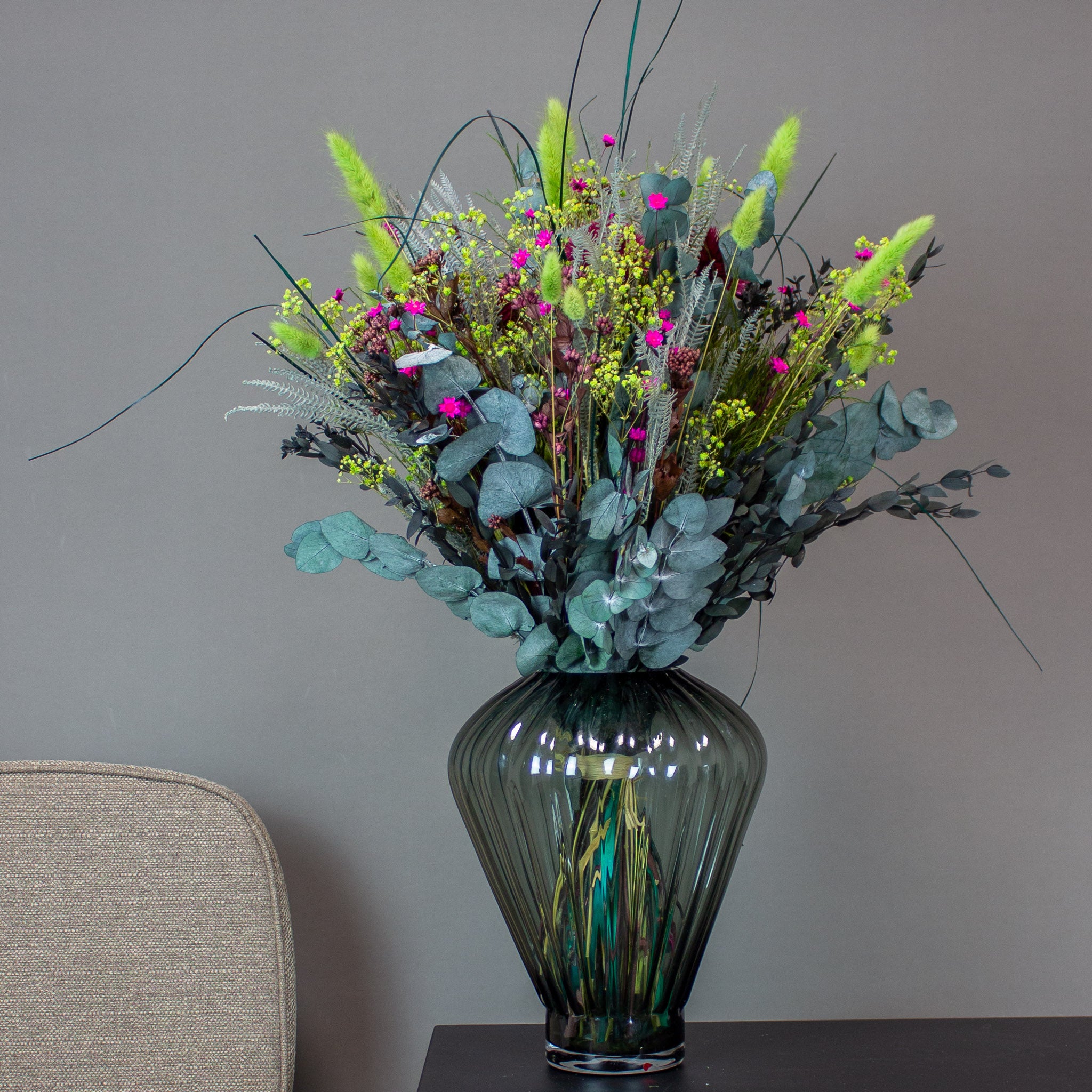Färgsprakande blombukett i gröna och rosa nyanser placerad i en grå glasvas.