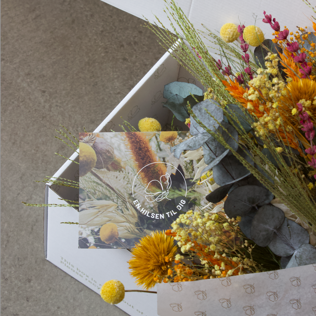 En gul och orange bukett som ligger fint nedpackad i silkespapper, i en vid låda.