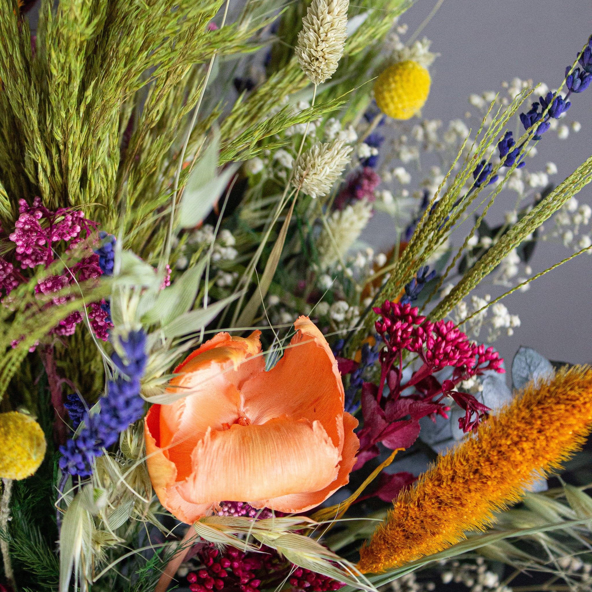 Nærbillede af en bukket med langtidsholdbare blomster i stærke farver, herunder orange, gul, lilla og grøn.