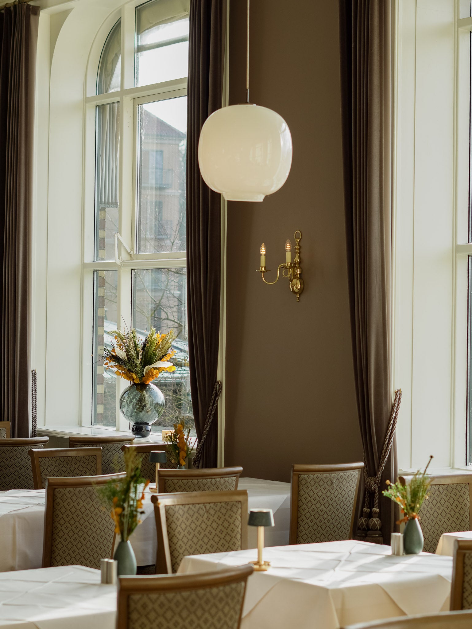 I hotellets spisesal står langtidsholdbare blomsterbuketter i forskellige størrelser på borde og vindueskarme.