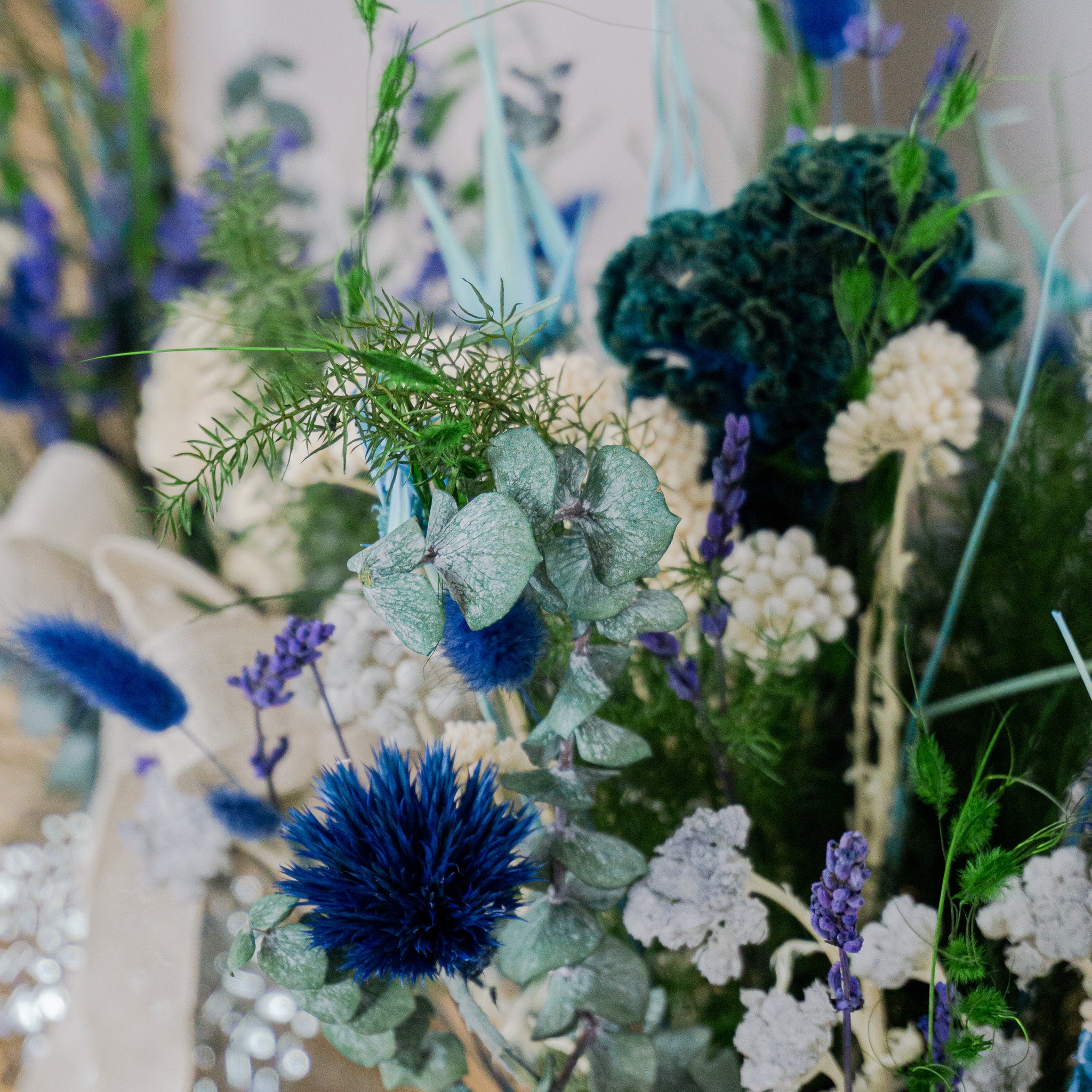 Nærbillede af en buket med holdbare blomster i blå, hvide og grønne nuancer.