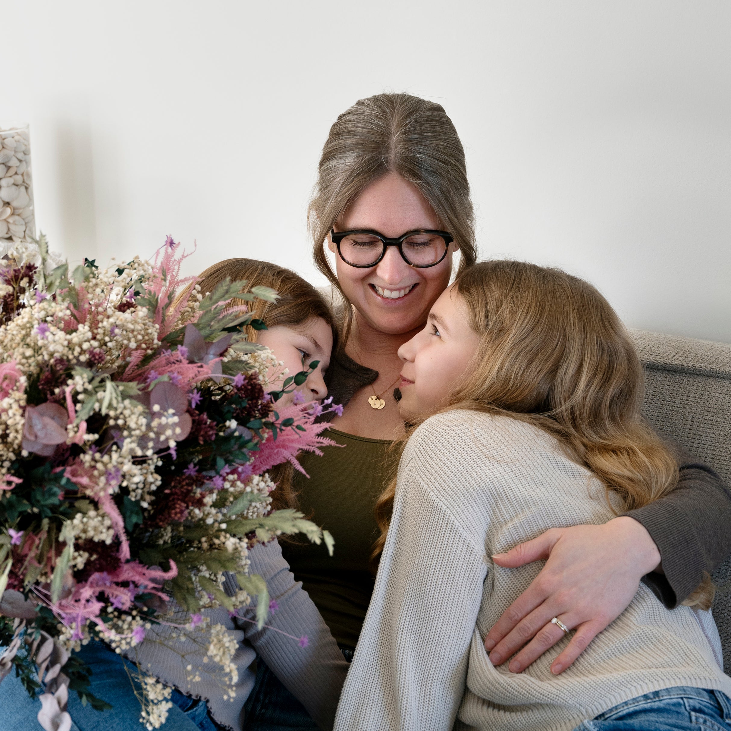 Mamma som ler när hennes barn omfamnar henne från båda sidorna efter att hon har fått en blombukett