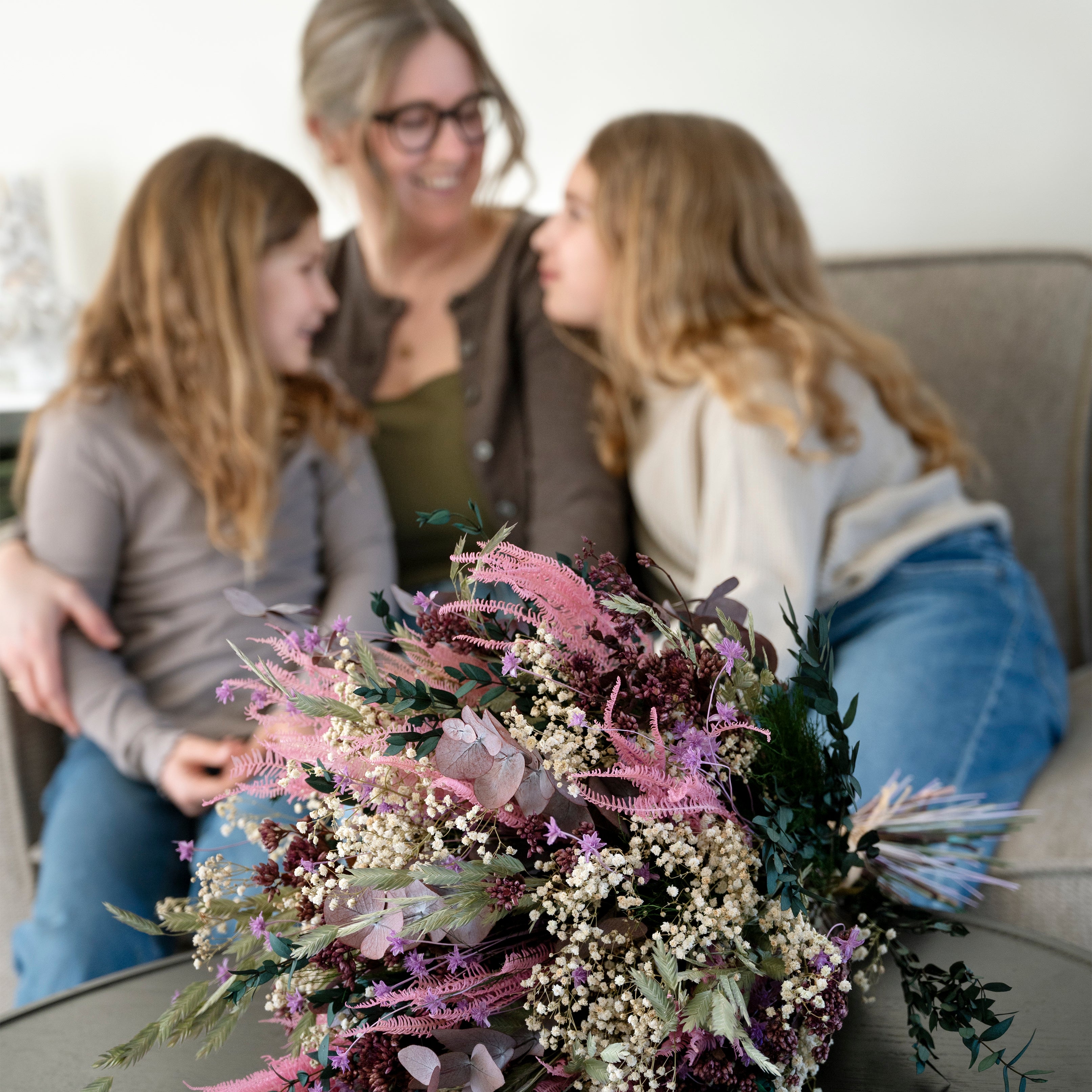 Närbild av en rosa och vit morsdagsbukett och mamma med två barn i bakgrunden