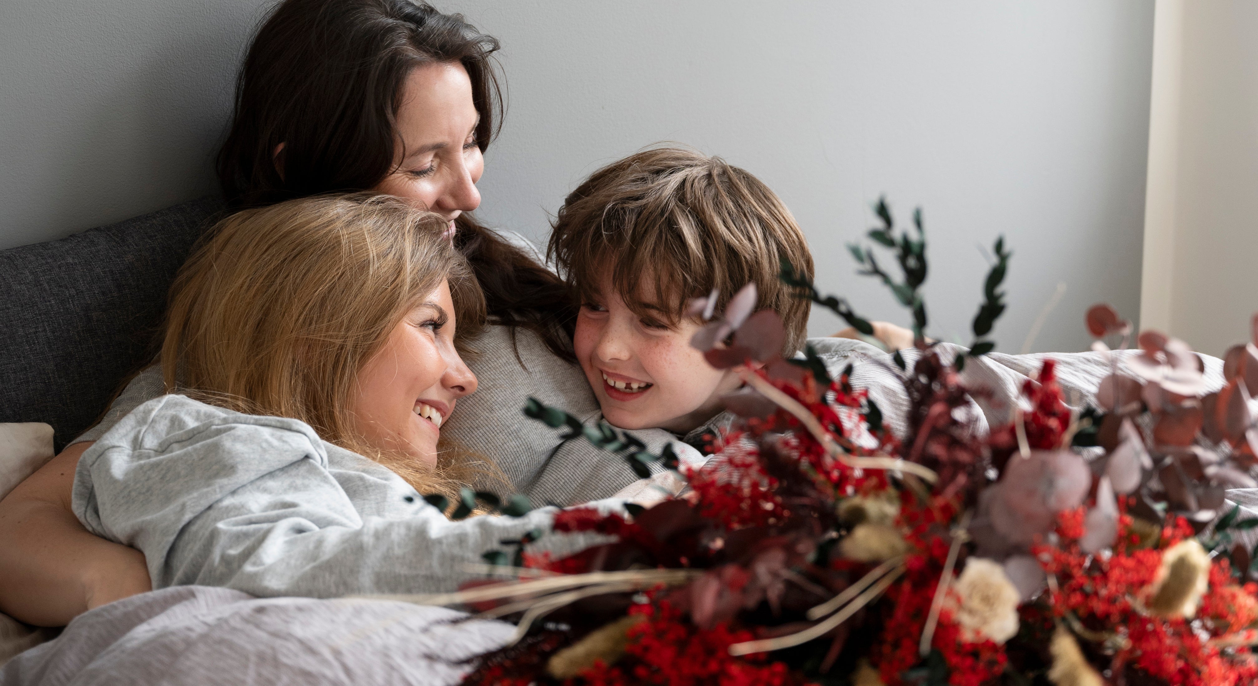 Mamma omringad av sina barn som har gett henne en blombukett på sängen