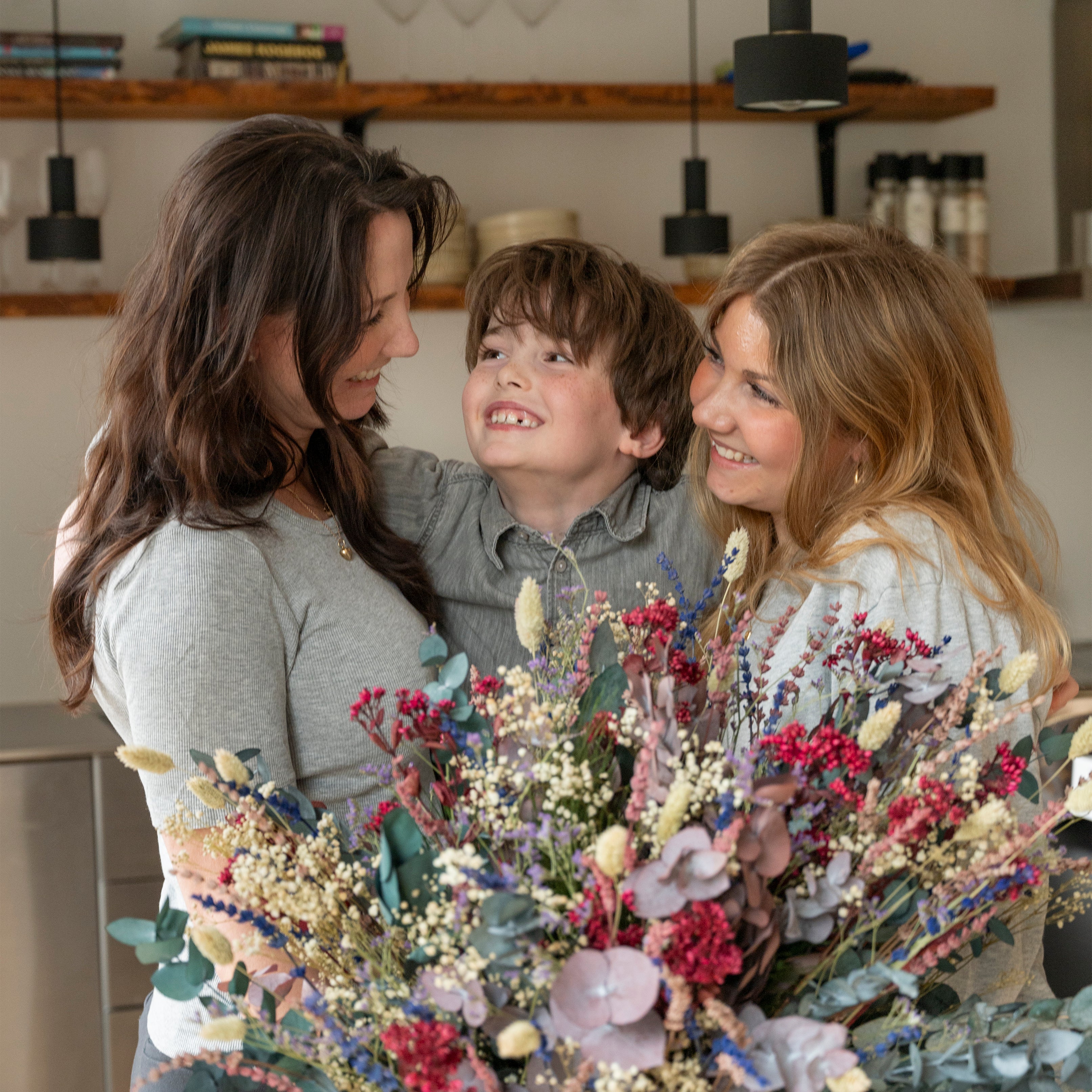 Mamma och barn som kramas i köket efter att amman fått en blombukett