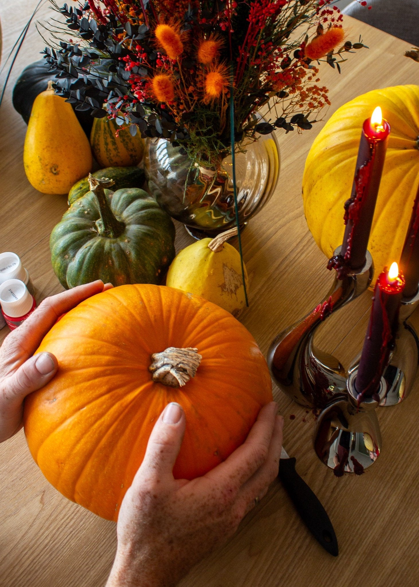Halloweenstämning med pumpor i olika former och färger som står på ett bord tillsammans med levande ljus och en orange blombukett