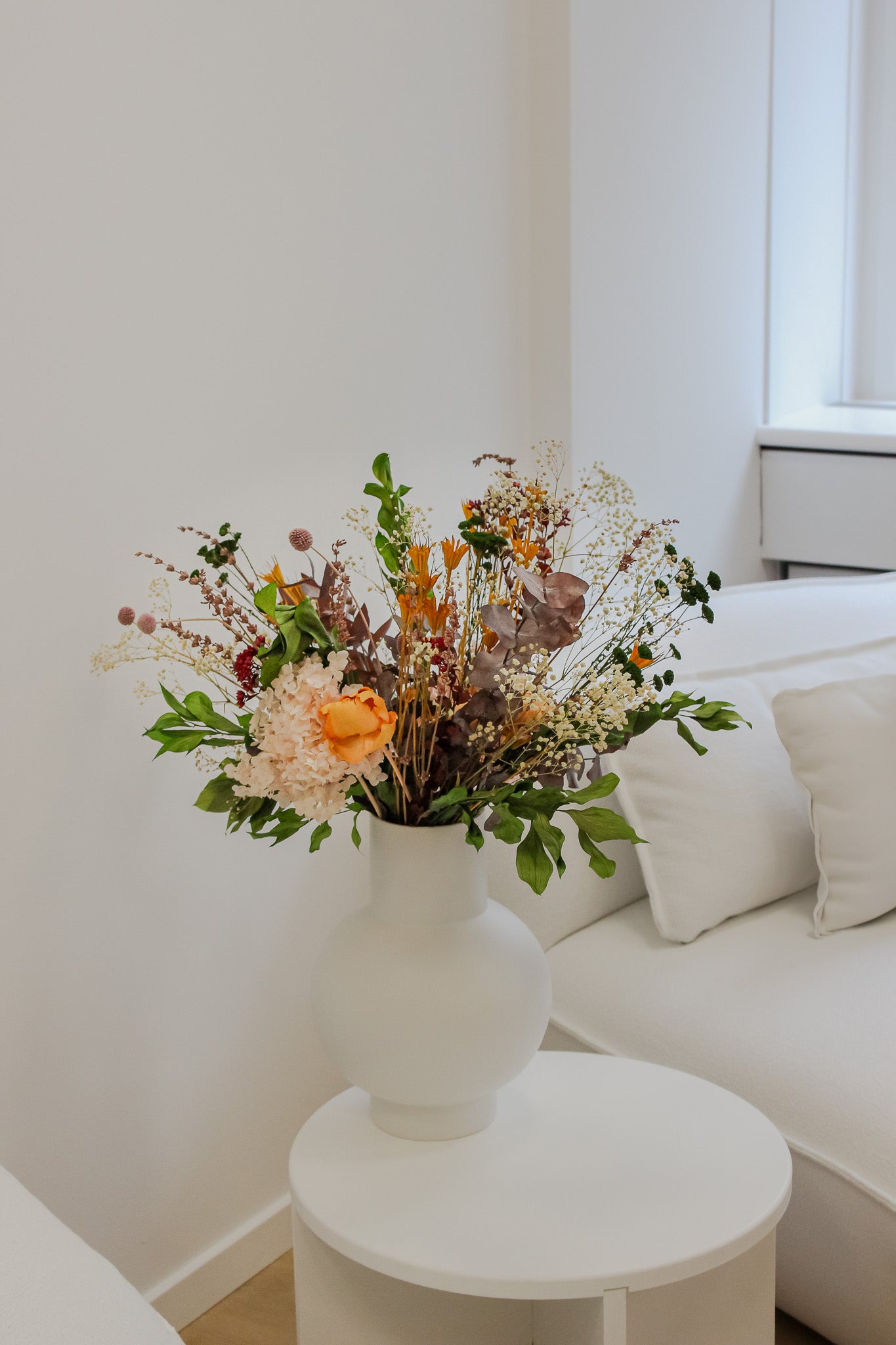 I et skandinavisk-minimalistisk indrettet hotelværelse står en farverig blomsterbuket på natbordet som et farverigt indslag i det hvidt holdte rum.